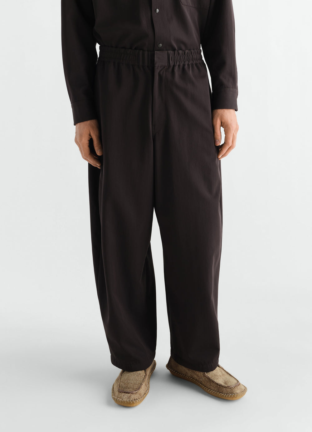 Jogger pants LEMAIRE black wool gabardine front worn by model with brown moccasin shoes