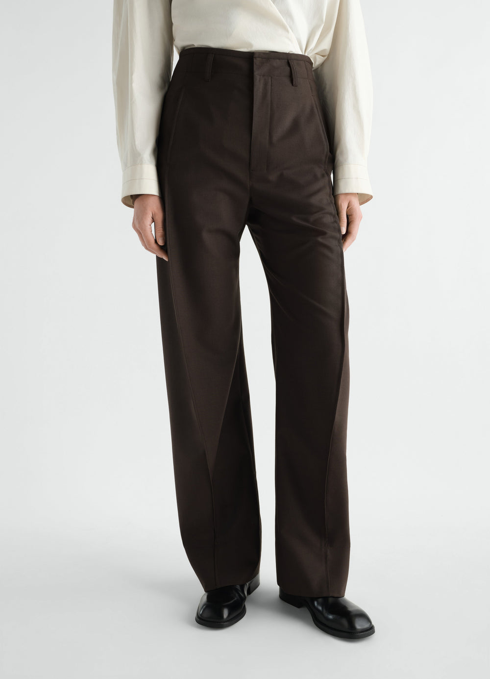 Baggy brown tropical wool blend pants by LEMAIRE worn by a model front view with black shoes and cream shirt