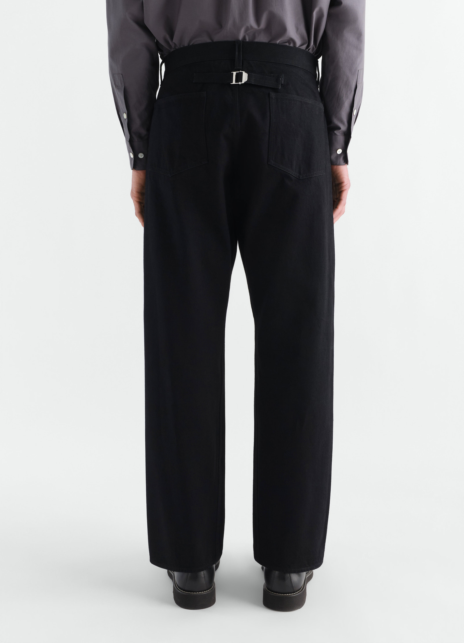 Straight black selvedge denim pants with back buckle detail worn by model, lemaire