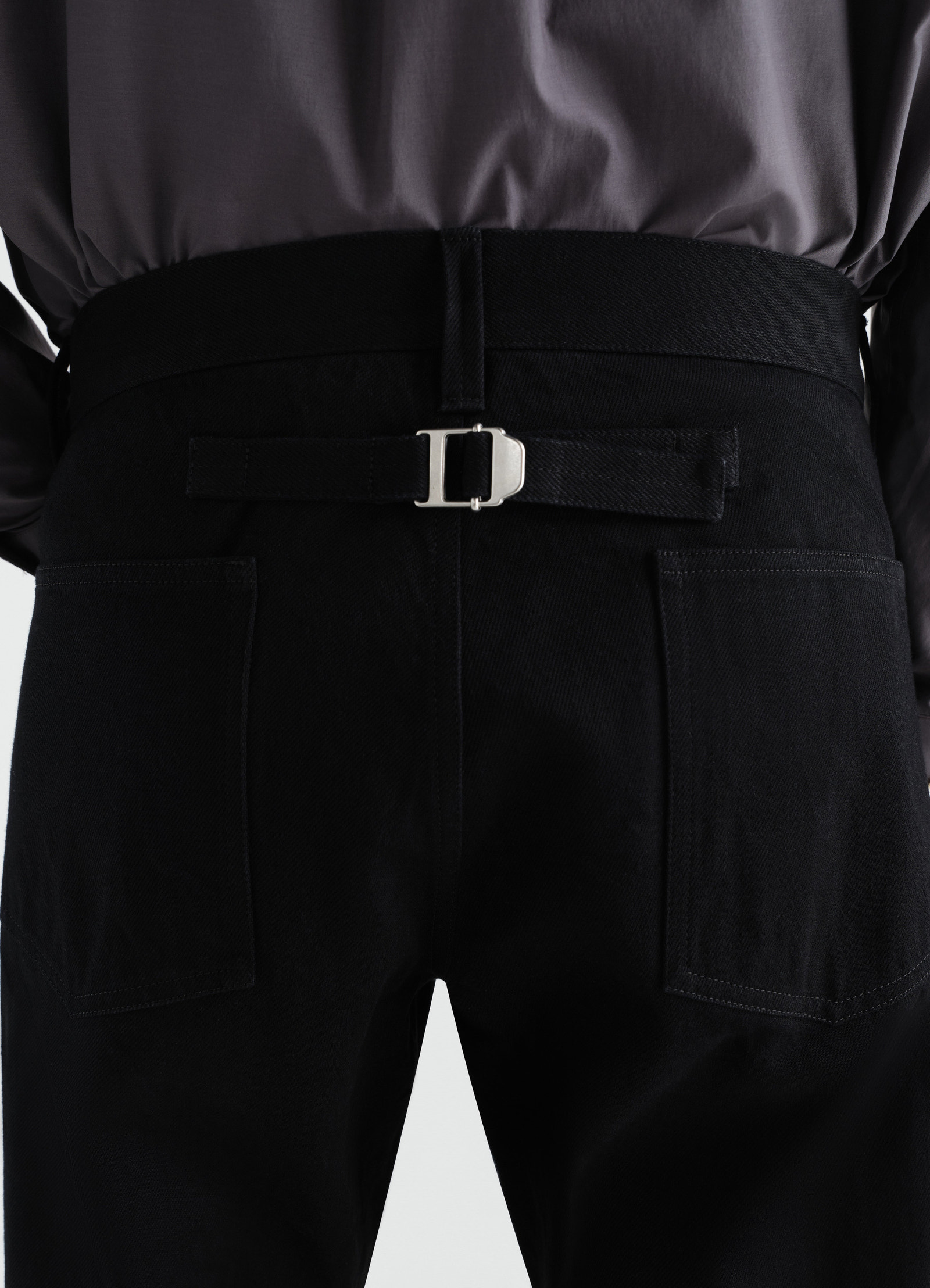 Straight five-pocket black selvedge denim pants by lemaire back close-up worn by model with buckle strap detail