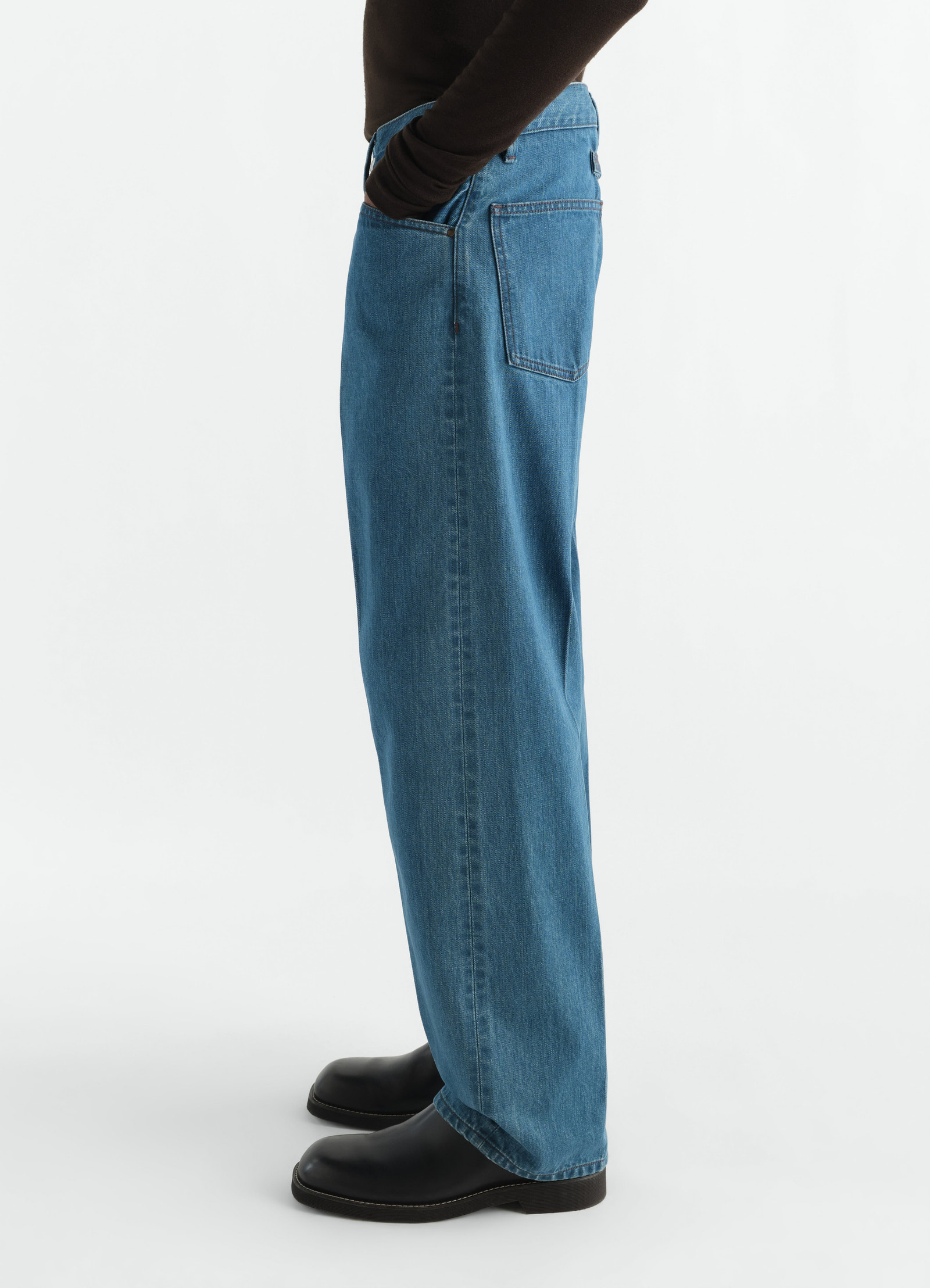Straight five-pocket indigo selvedge denim pants lemaire worn by a model side view with black boots and brown top