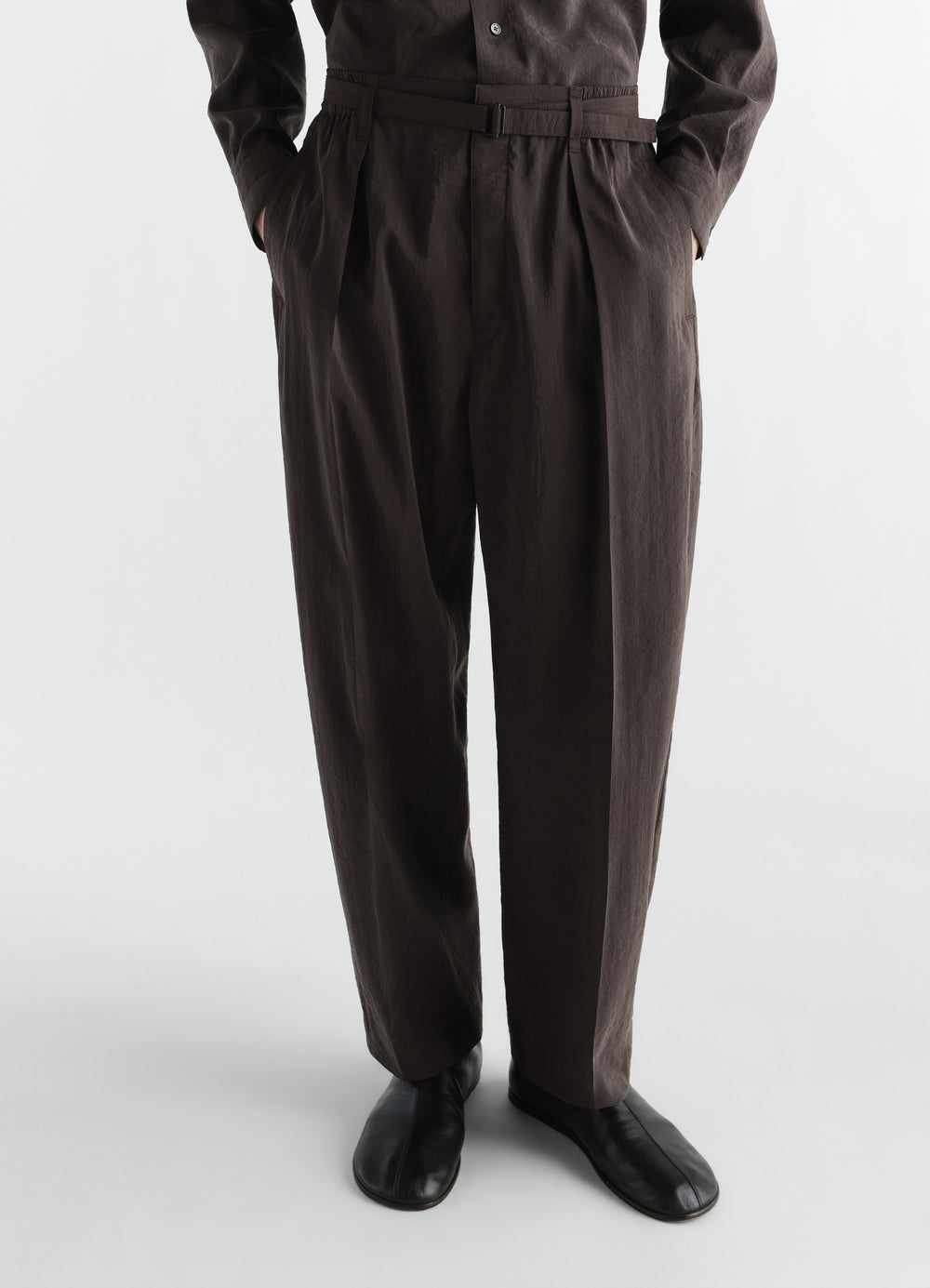 Belted relaxed brown dry silk pants by LEMAIRE worn by a model front view with pockets and black shoes