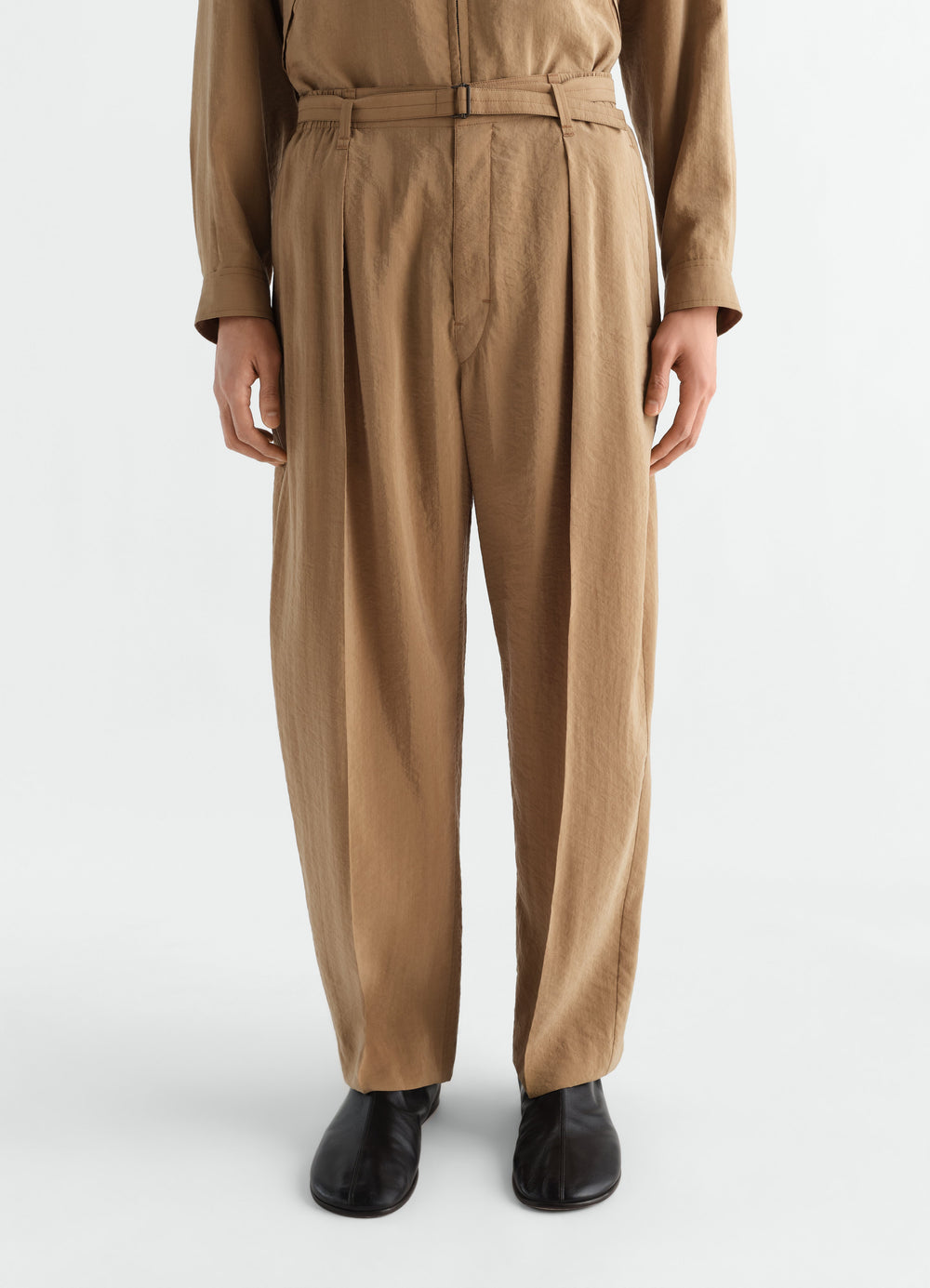 Belted relaxed dry silk pants in brown by LEMAIRE worn by model front view with black shoes