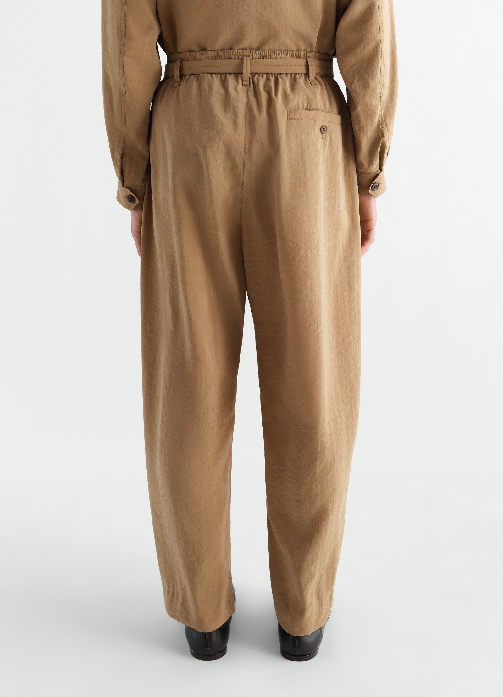 Belted relaxed dry silk pants in tan brown by lemaire worn by a model back view with button pocket detail