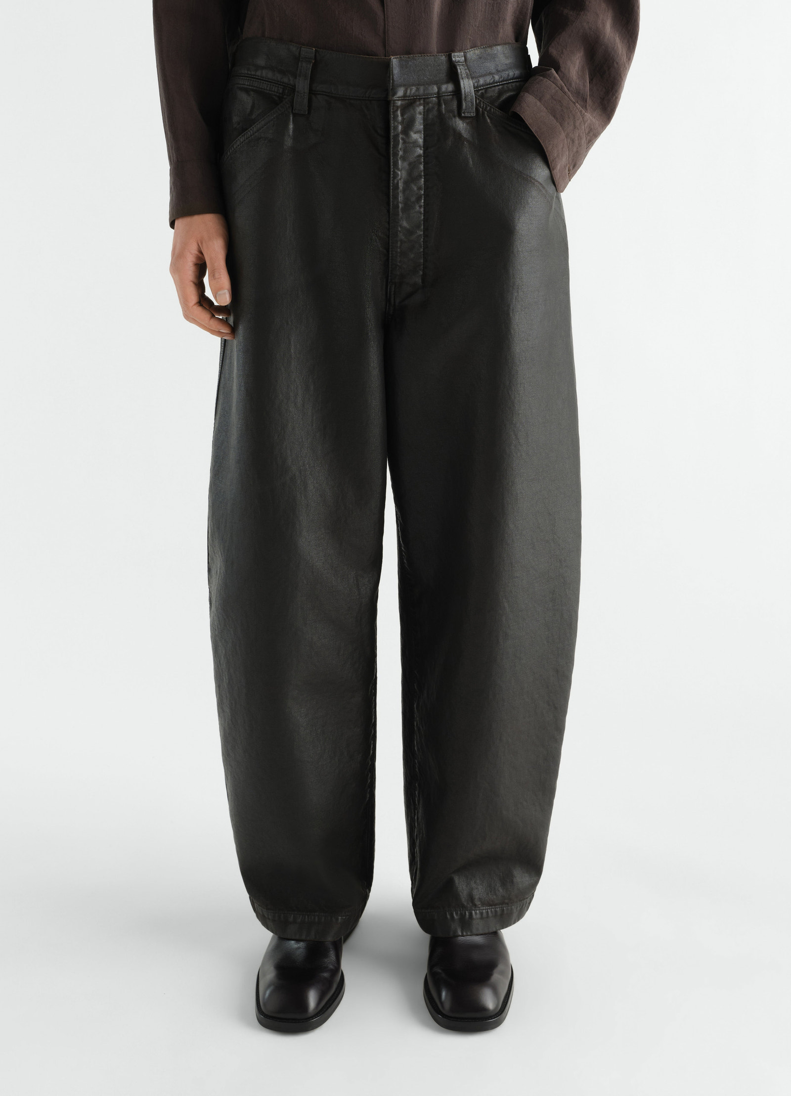 Oversized black coated denim pants by lemaire worn by model front view with pockets and belt loops