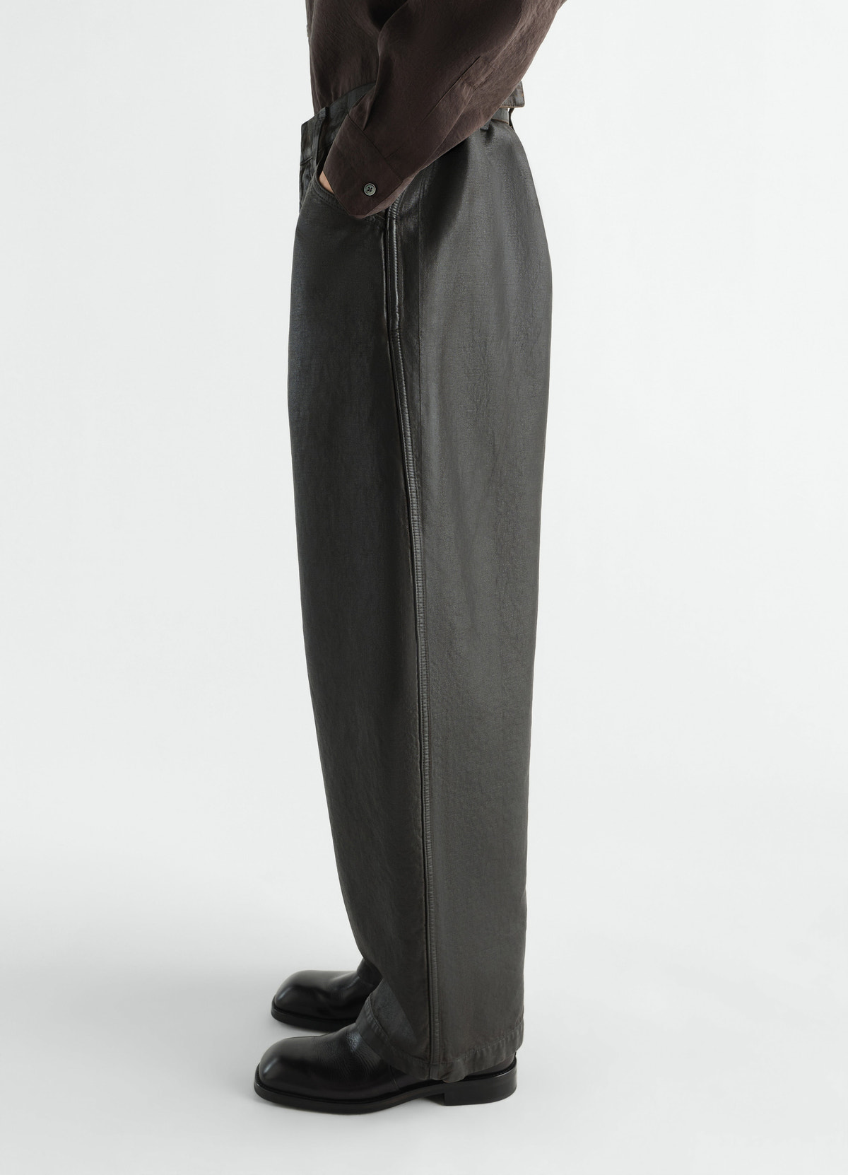 Oversized black coated denim pants by lemaire worn by model side view with black boots and brown shirt