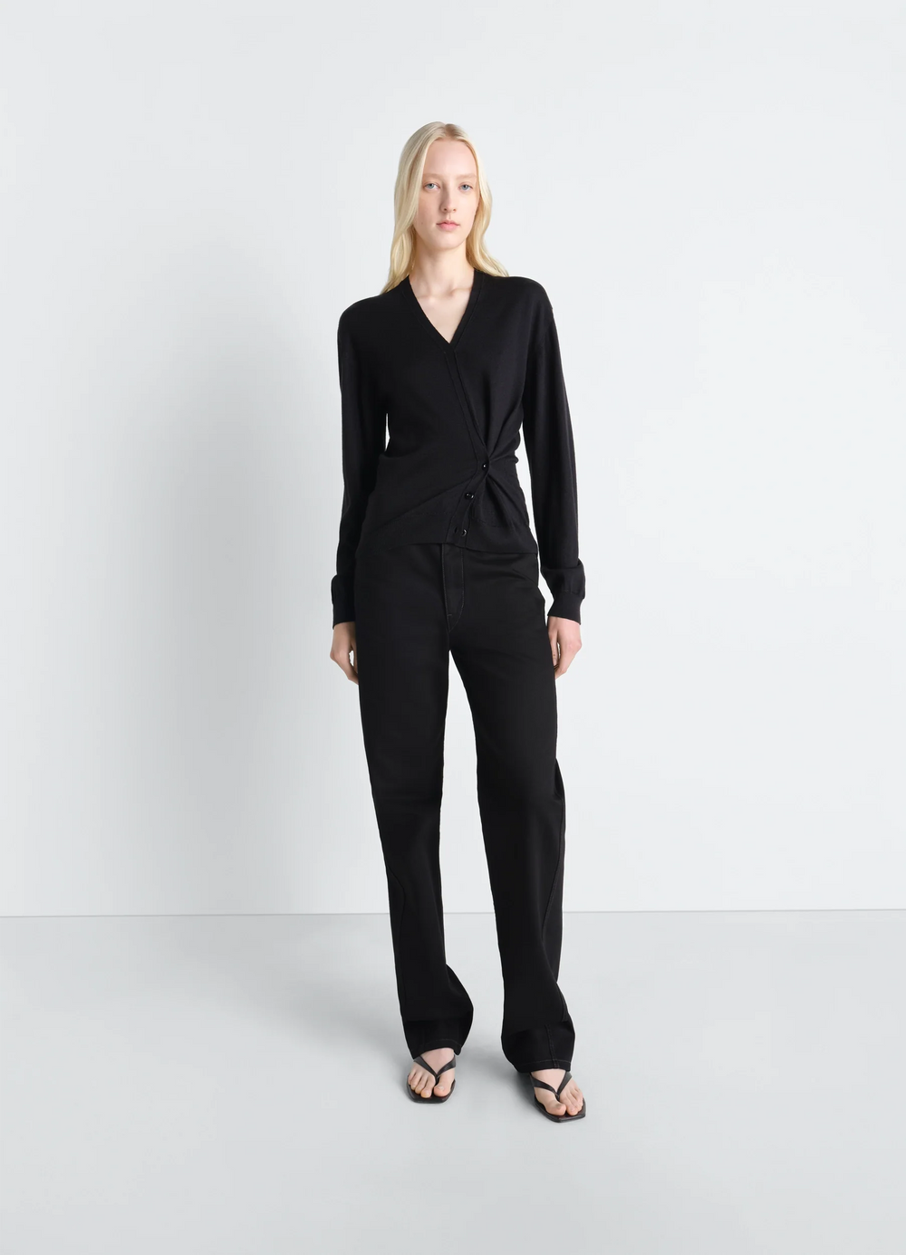 TWISTED V NECK JUMPER in Black Merino Blend, model shot, three-quarter view asymmetrical hem detail