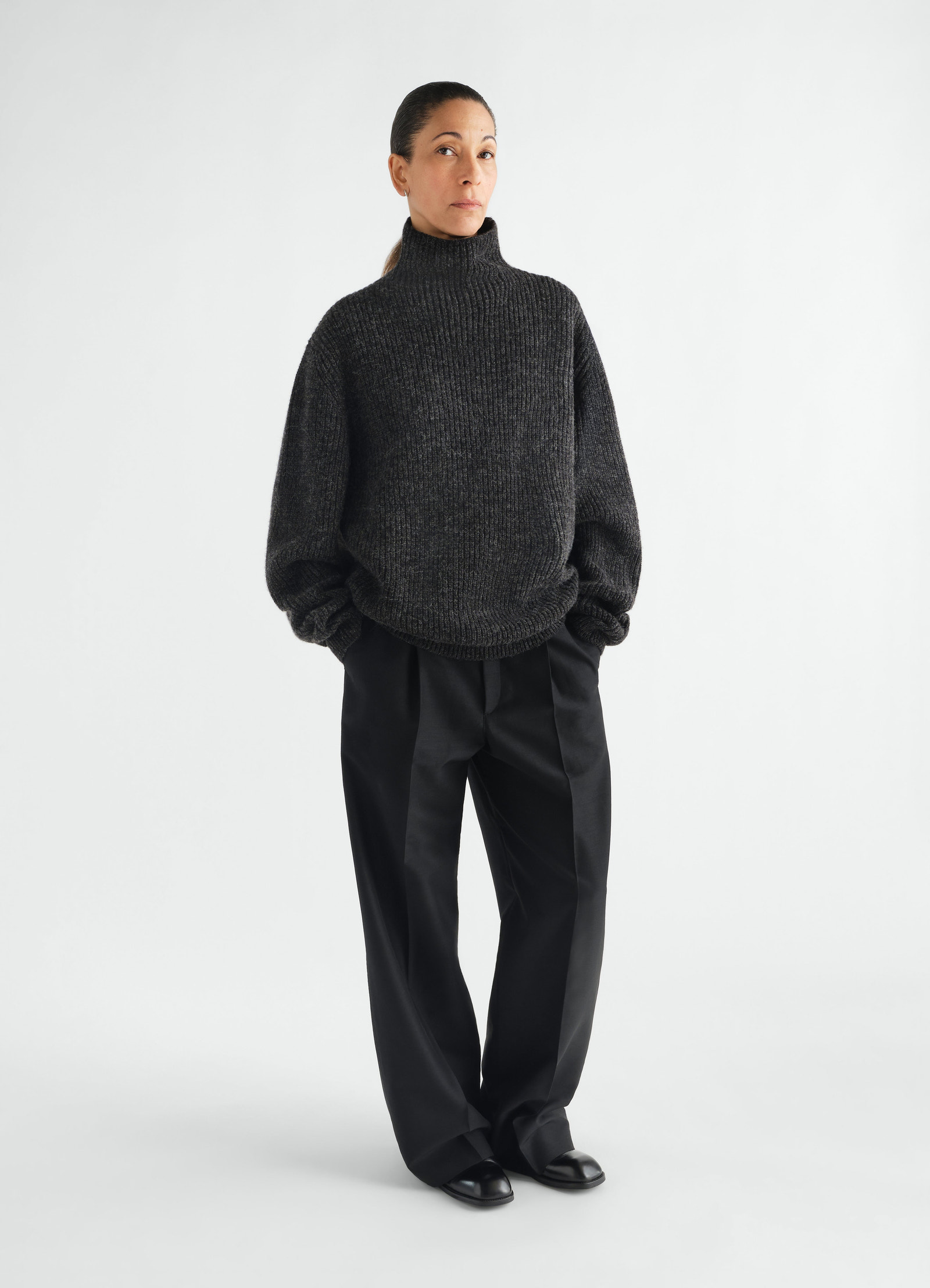 High neck dark grey yak alpaca sweater by lemaire worn by a model with black trousers on white background