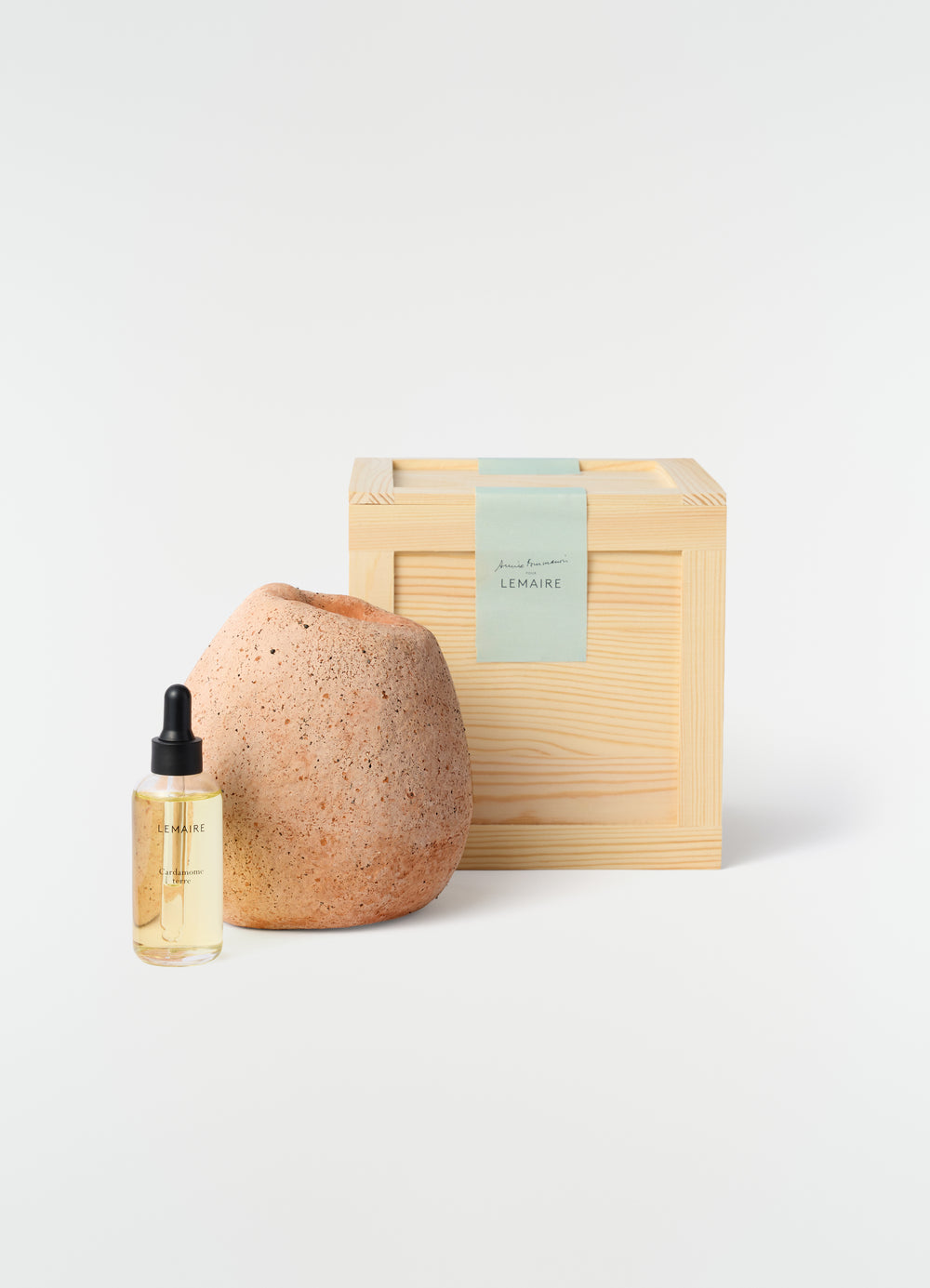 LEMAIRE skincare set with clear glass dropper bottle, textured clay vase, and light wood box on white background