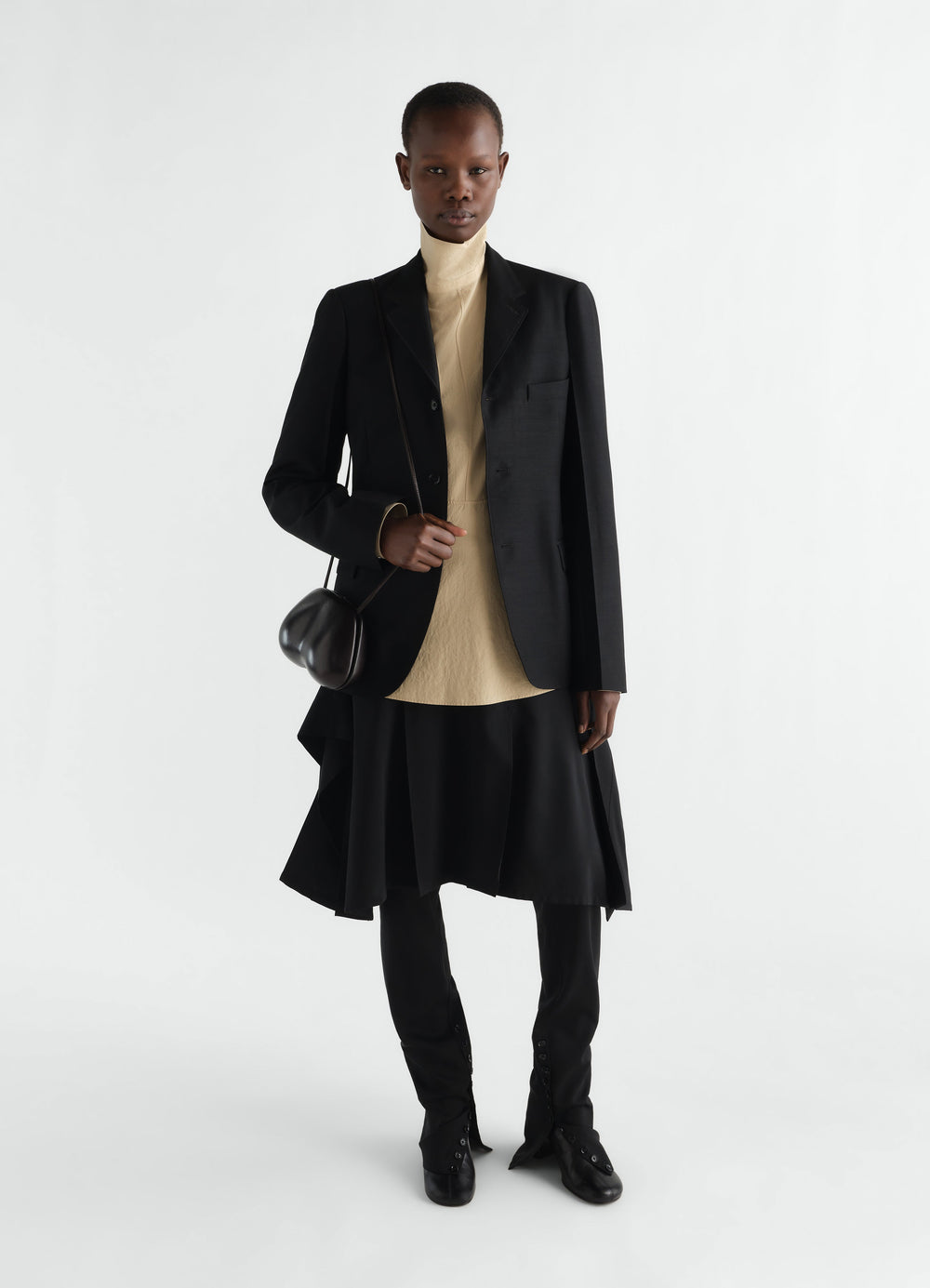 Press-stud bib top in beige cotton crepe styled with black blazer and skirt worn by model LEMAIRE
