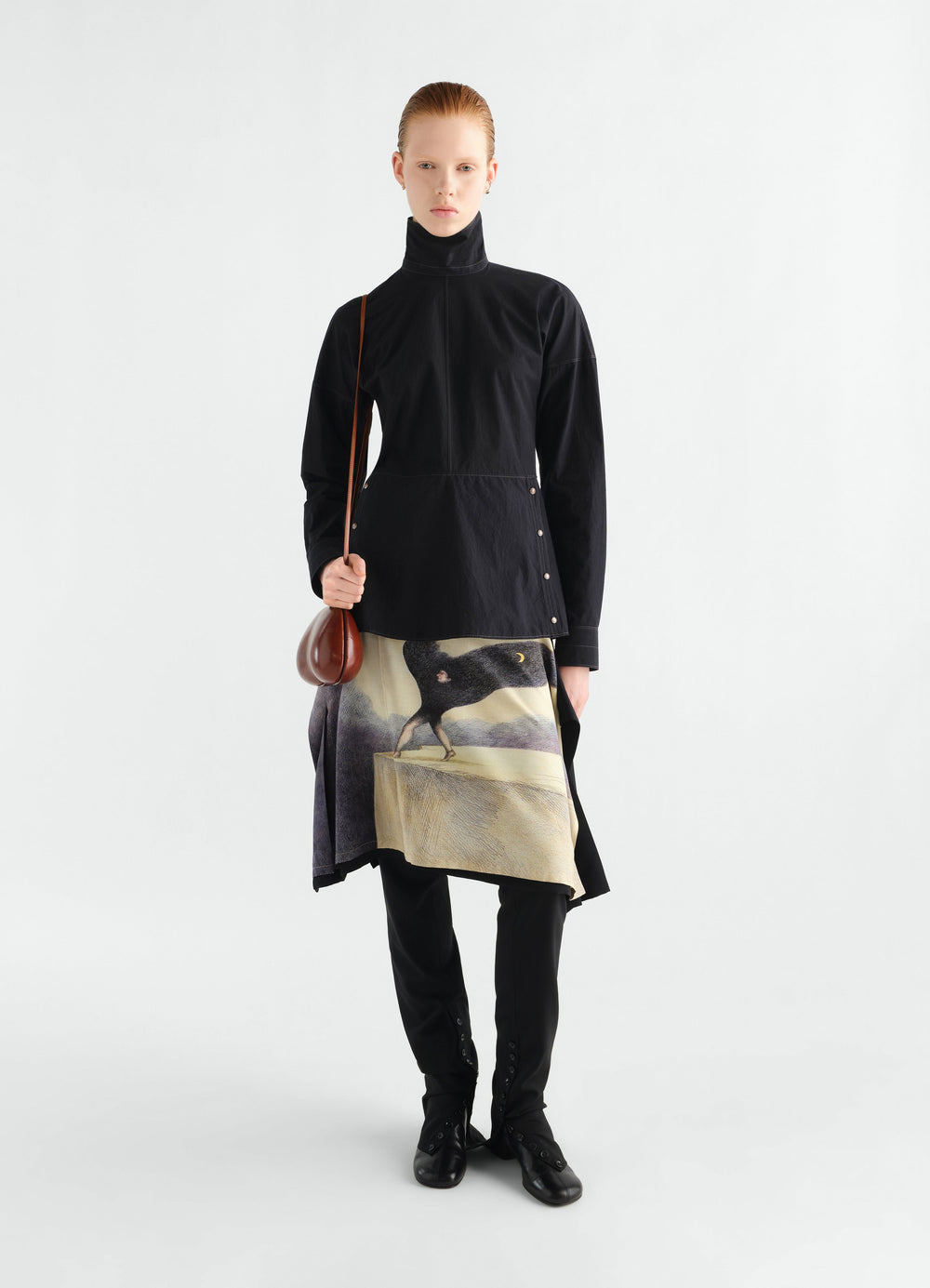 Press-stud black cotton crepe bib top by LEMAIRE worn by model with printed skirt and brown shoulder bag front view