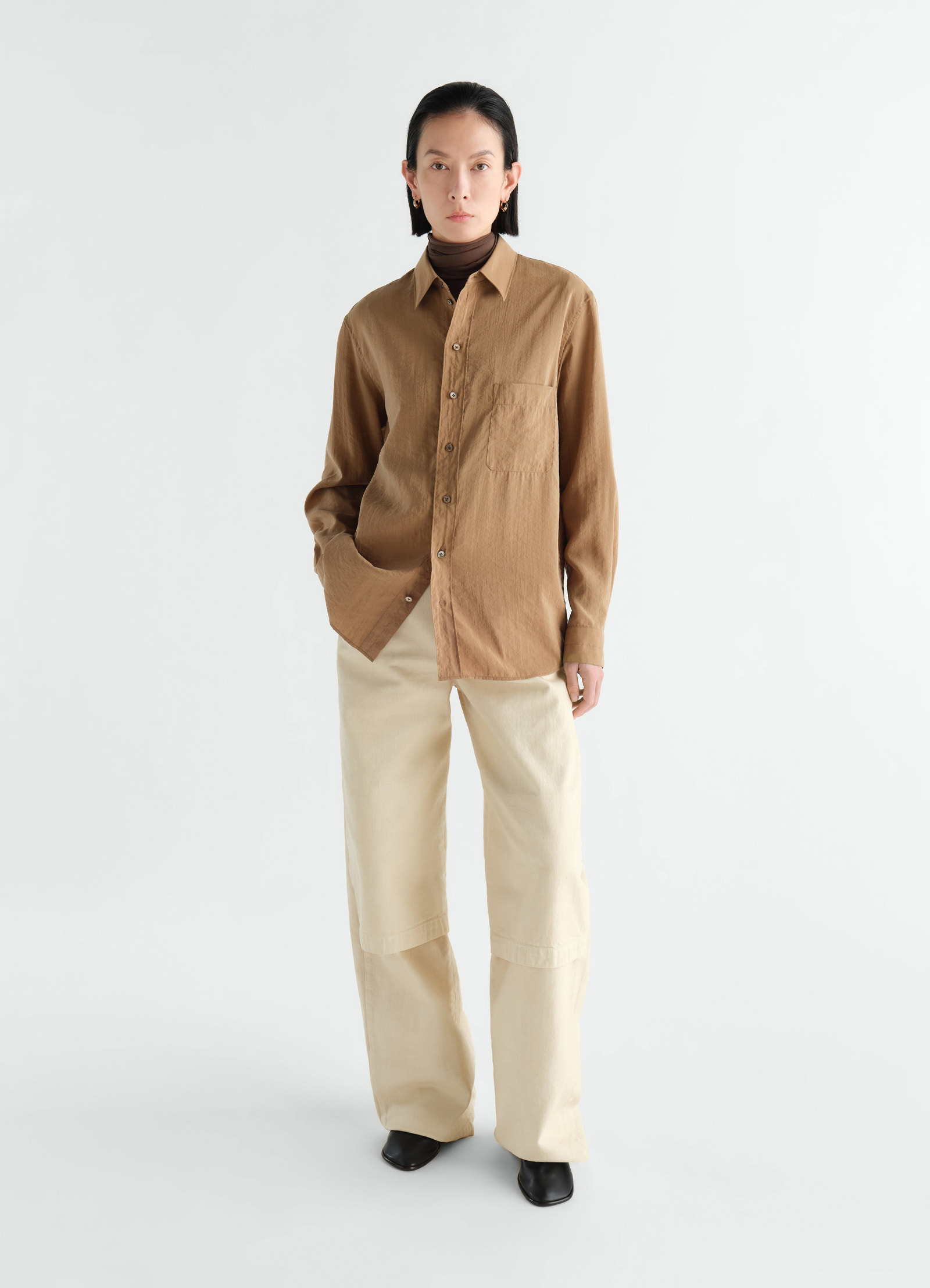 Straight brown dry silk shirt by lemaire worn by a model with cream pants against white background