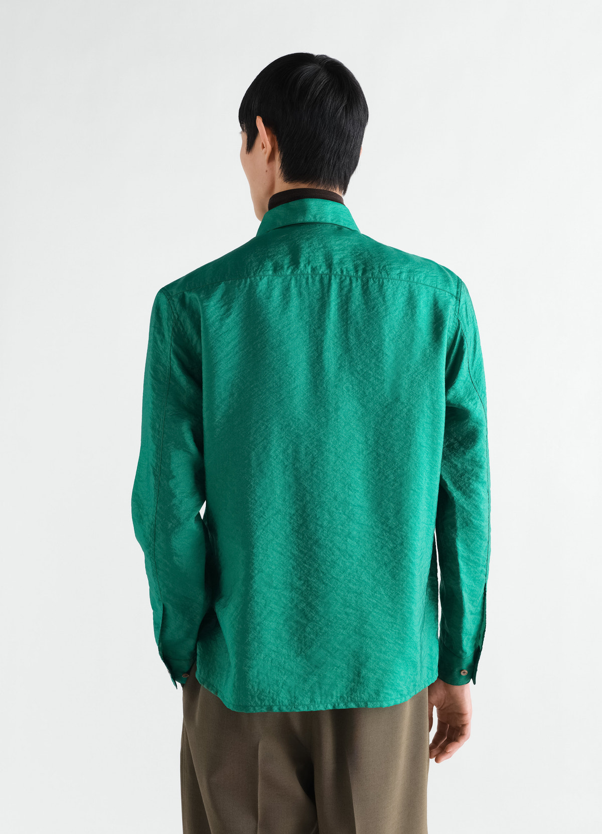 Fitted green shiny cupro shirt by lemaire worn by a model back view with long sleeves and buttoned cuffs