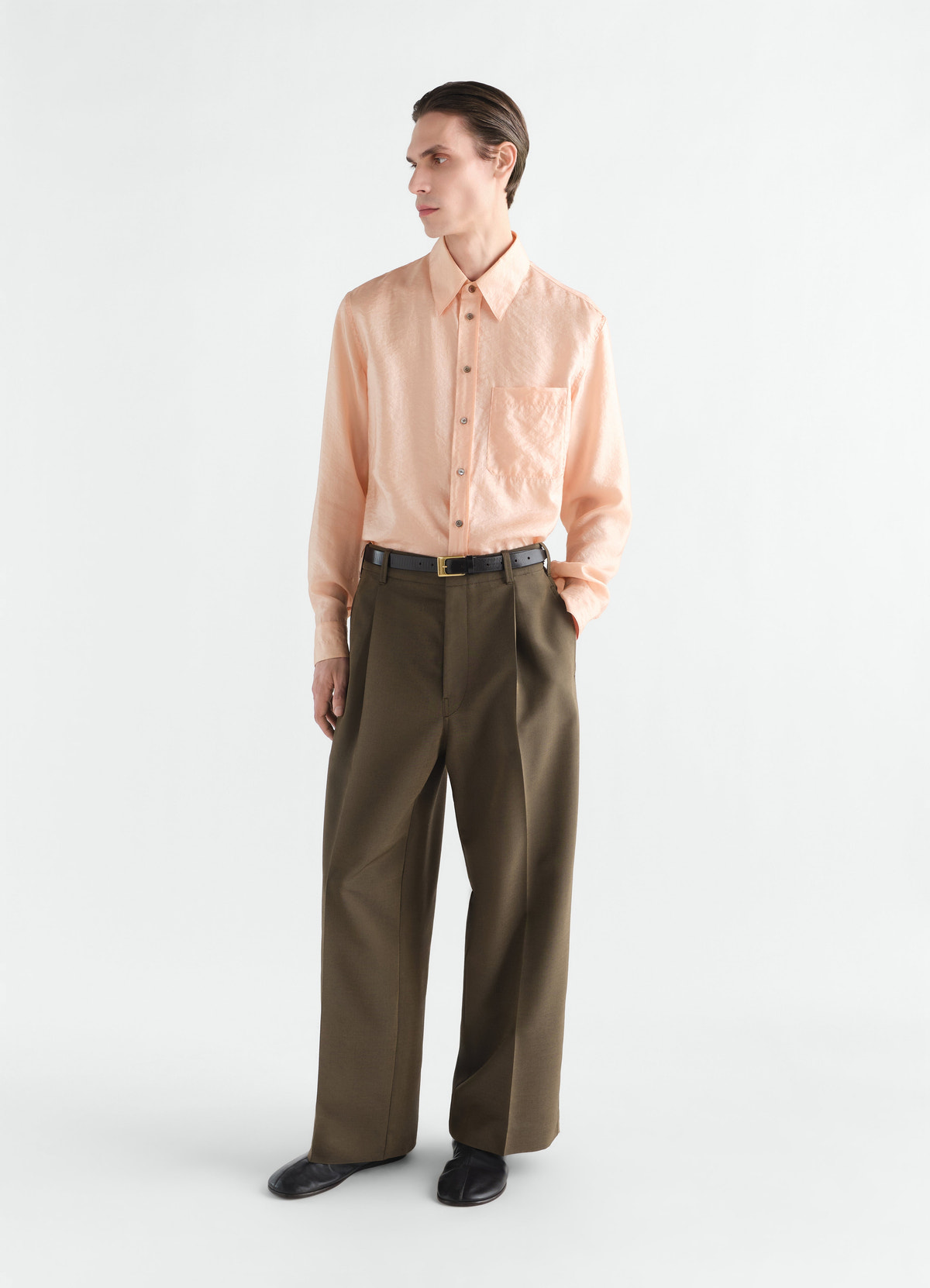 Fitted peach shiny cupro shirt by lemaire worn by model with olive wide trousers side view