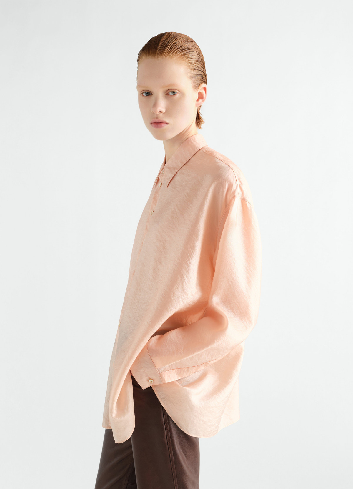 Draped peach shiny cupro shirt by lemaire worn by a model side view with long sleeves and collar