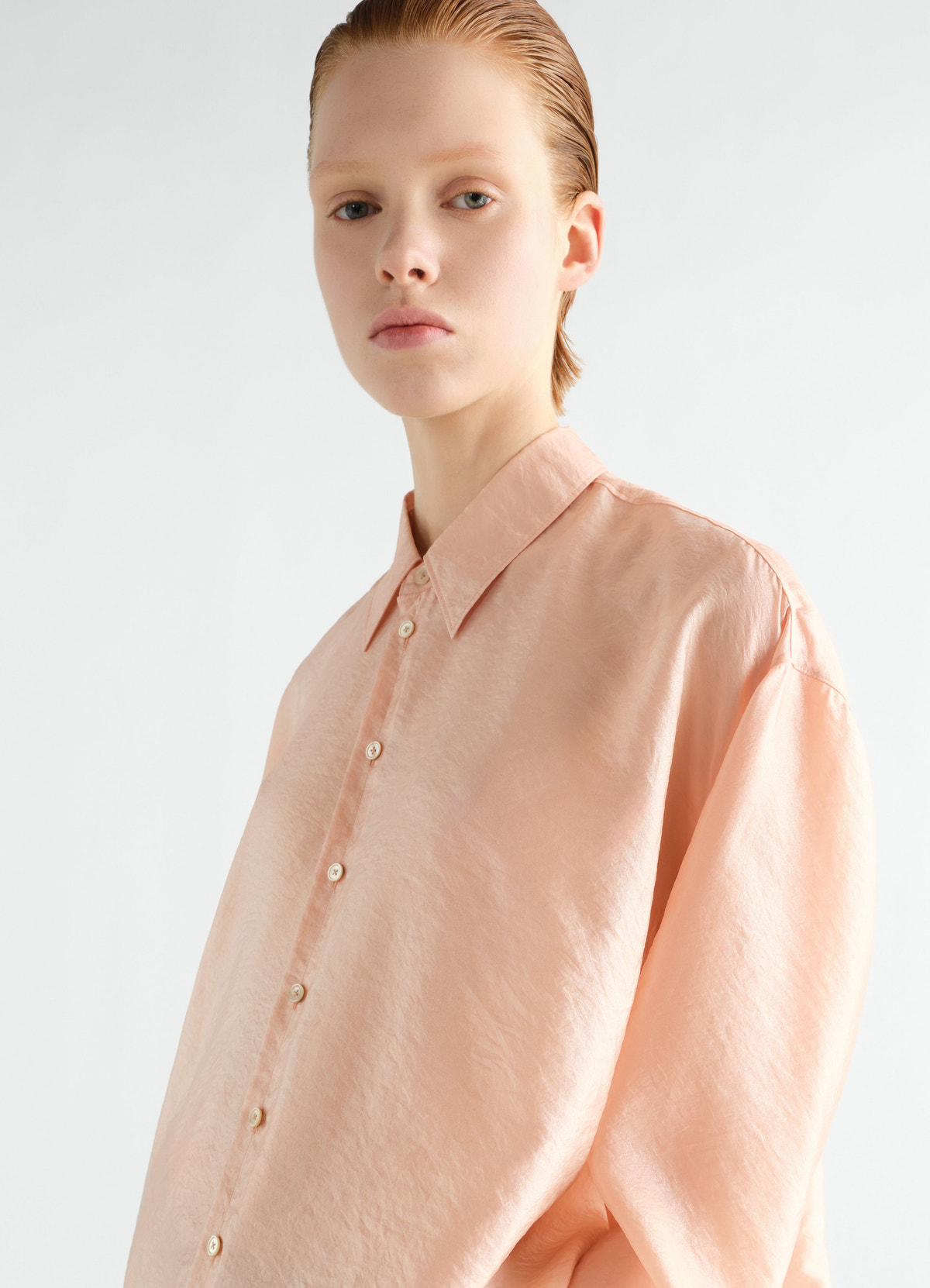 Draped shiny peach cupro shirt by lemaire worn by model front view with collar and button details
