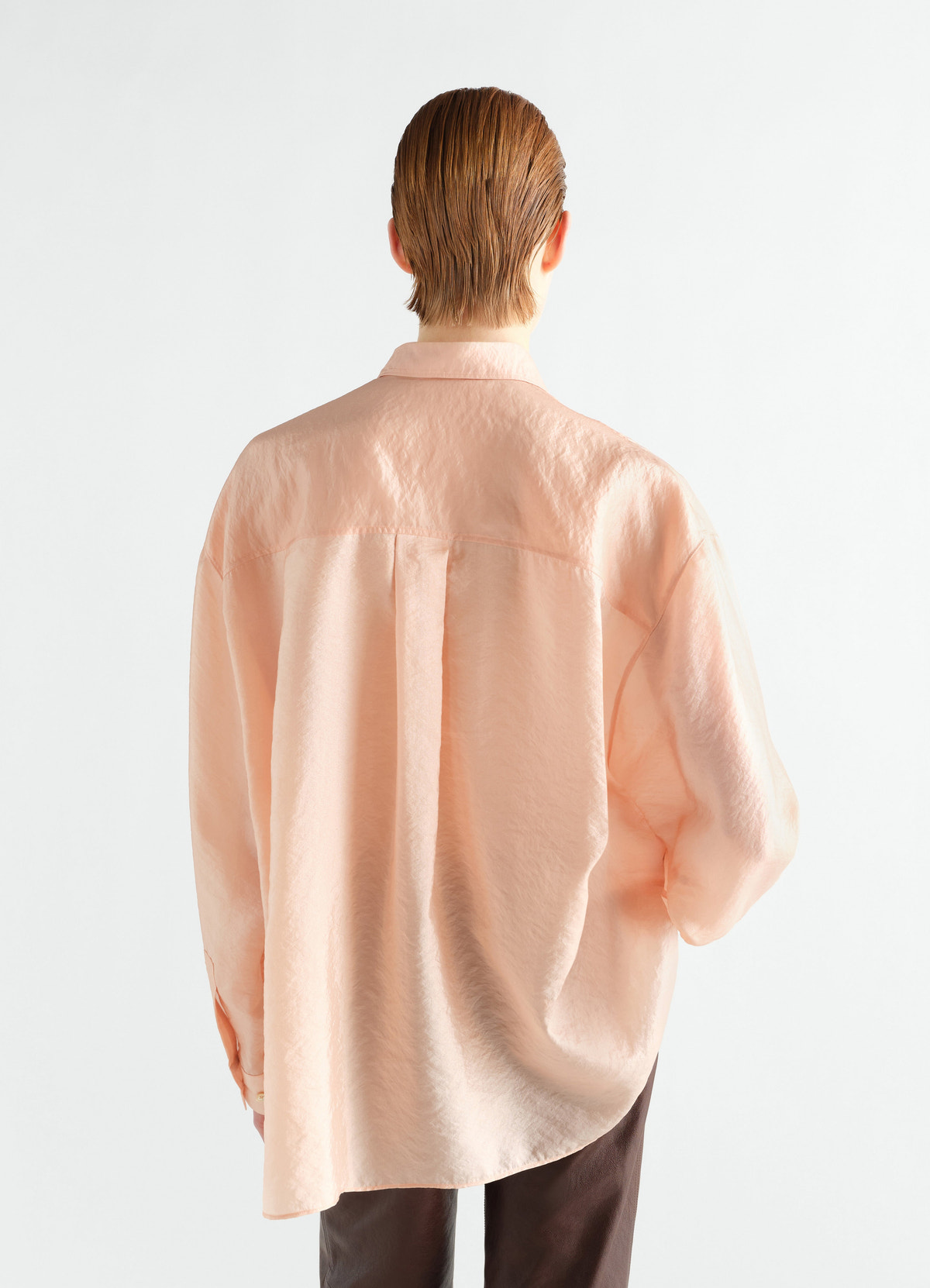 Draped peach shiny cupro shirt by lemaire worn by model, back view against plain white background