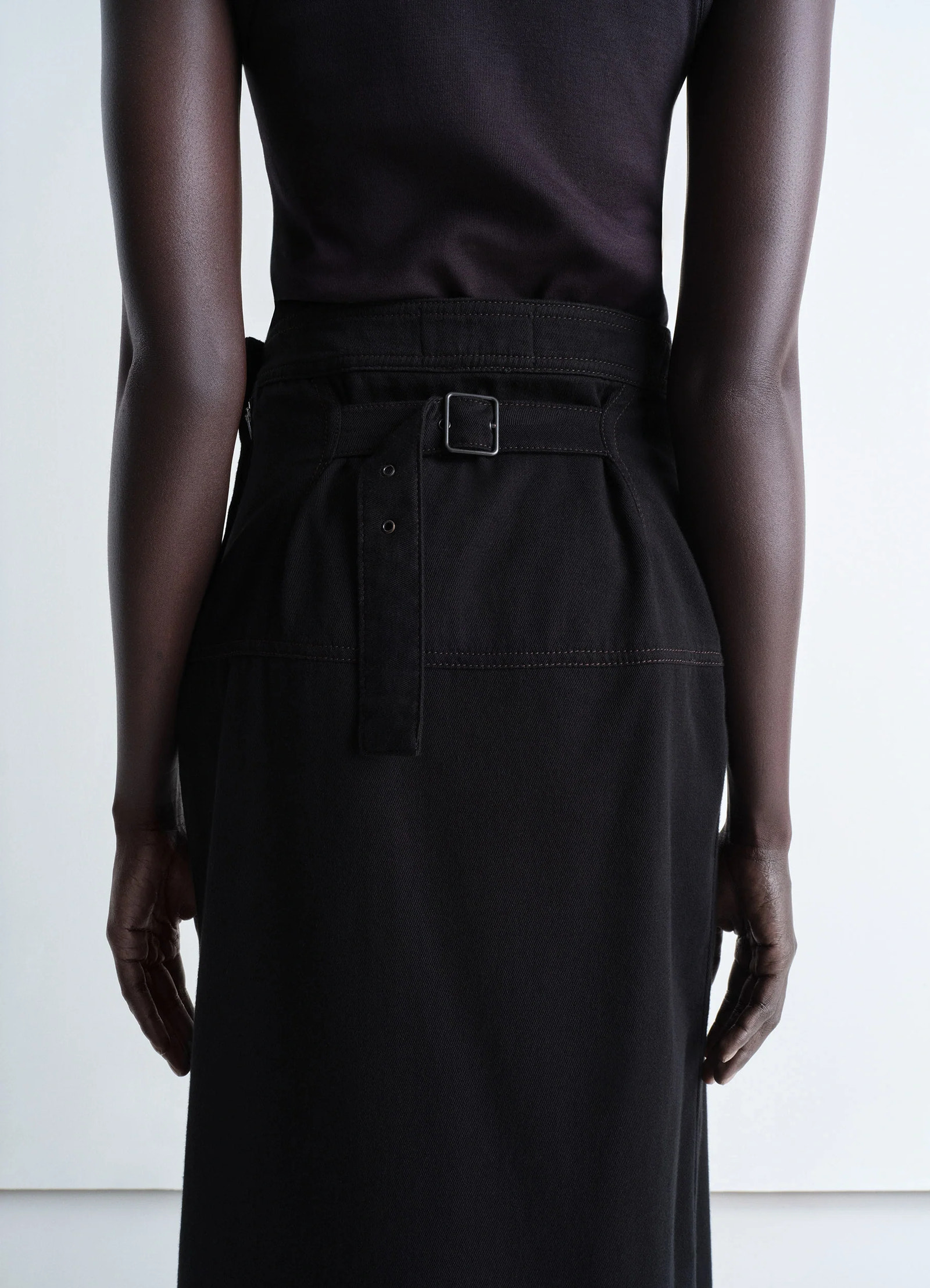 Lemaire asymmetrical wrap skirt in black cotton denim, model shot, back view belt with buckle, fitted cut