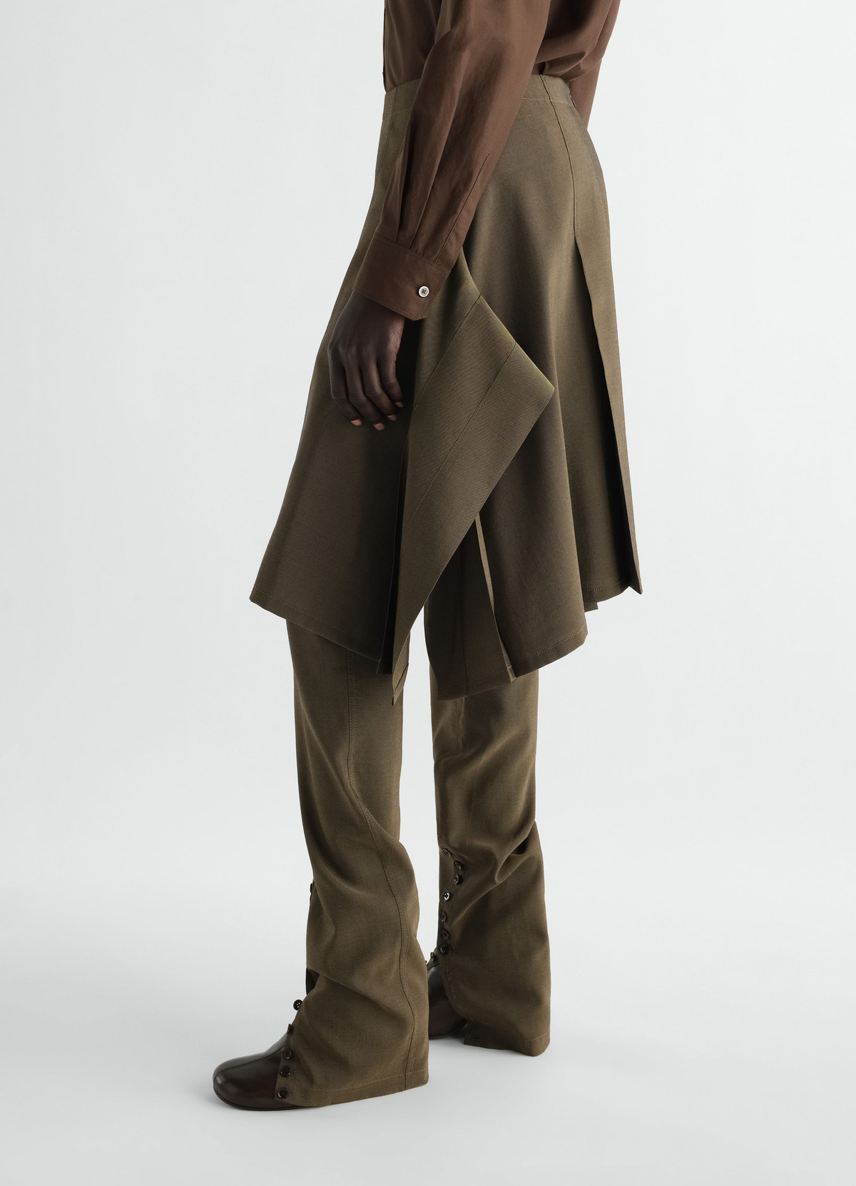 Pleated brown wool and mohair skirt layered over trousers worn by model lemaire side view
