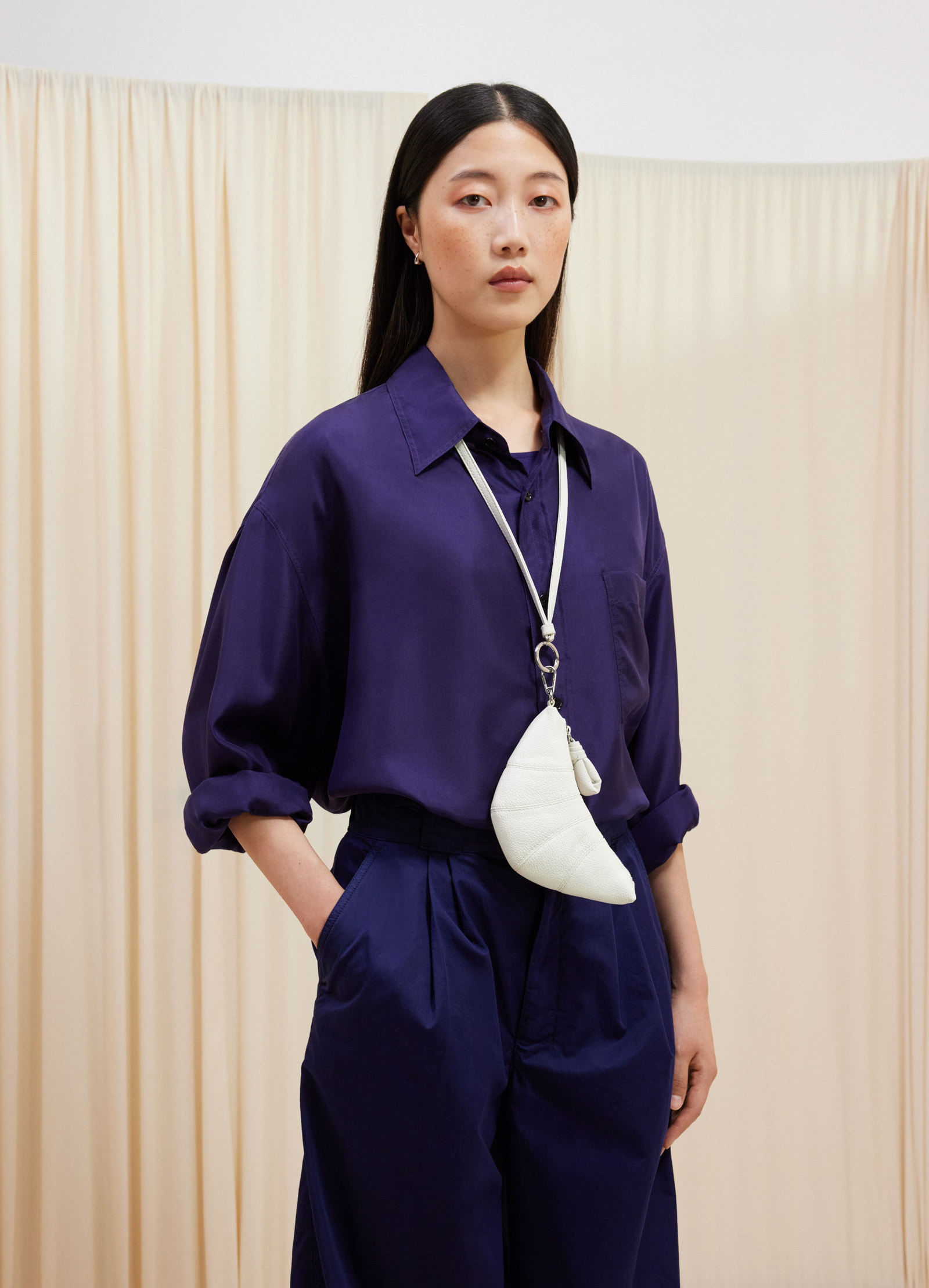 Croissant coin purse necklace in soft grained leather, model shot, worn front view hanging from neck strap