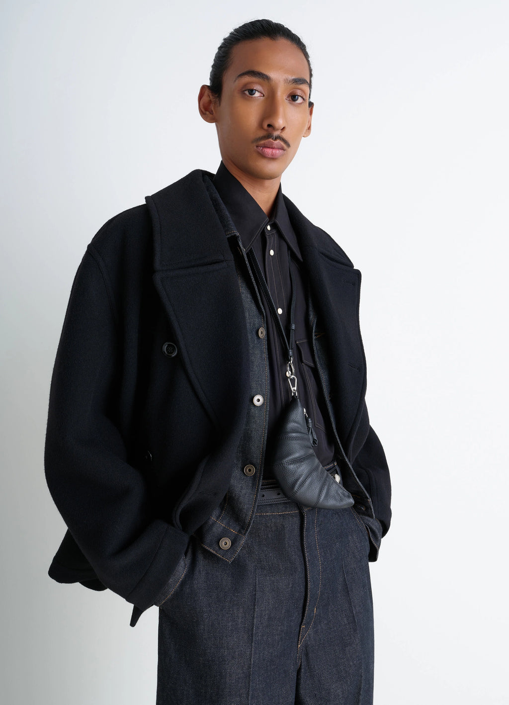 CROSS-BODY CROISSANT COIN PURSE in black grained leather, model shot, front view worn crossbody