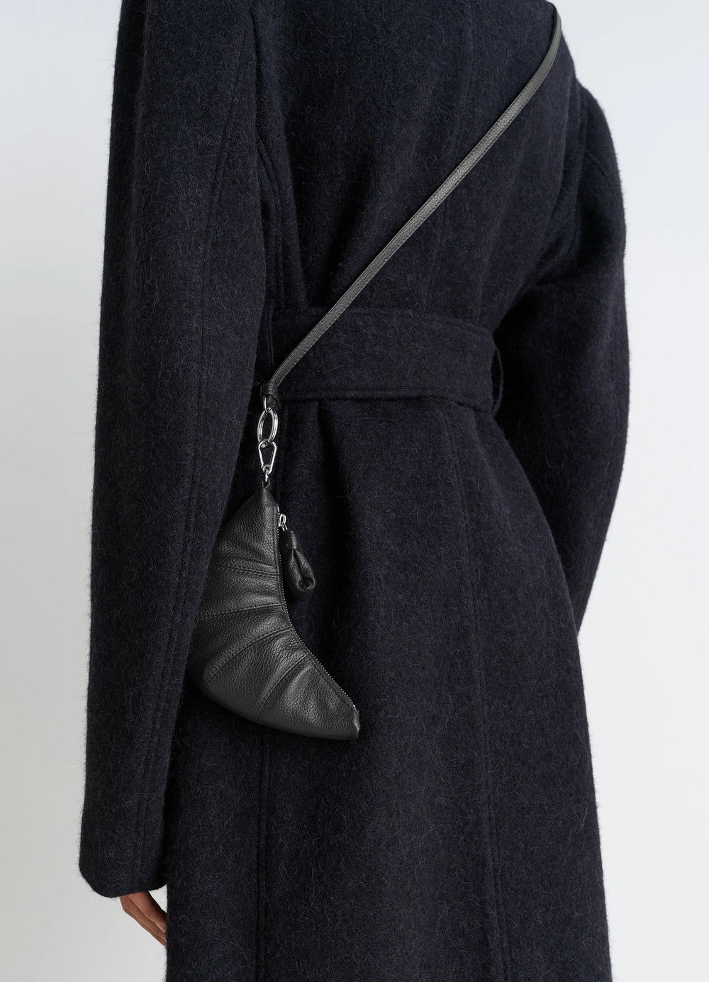 CROSS-BODY CROISSANT COIN PURSE in black grained leather, model shot, side view hanging pose