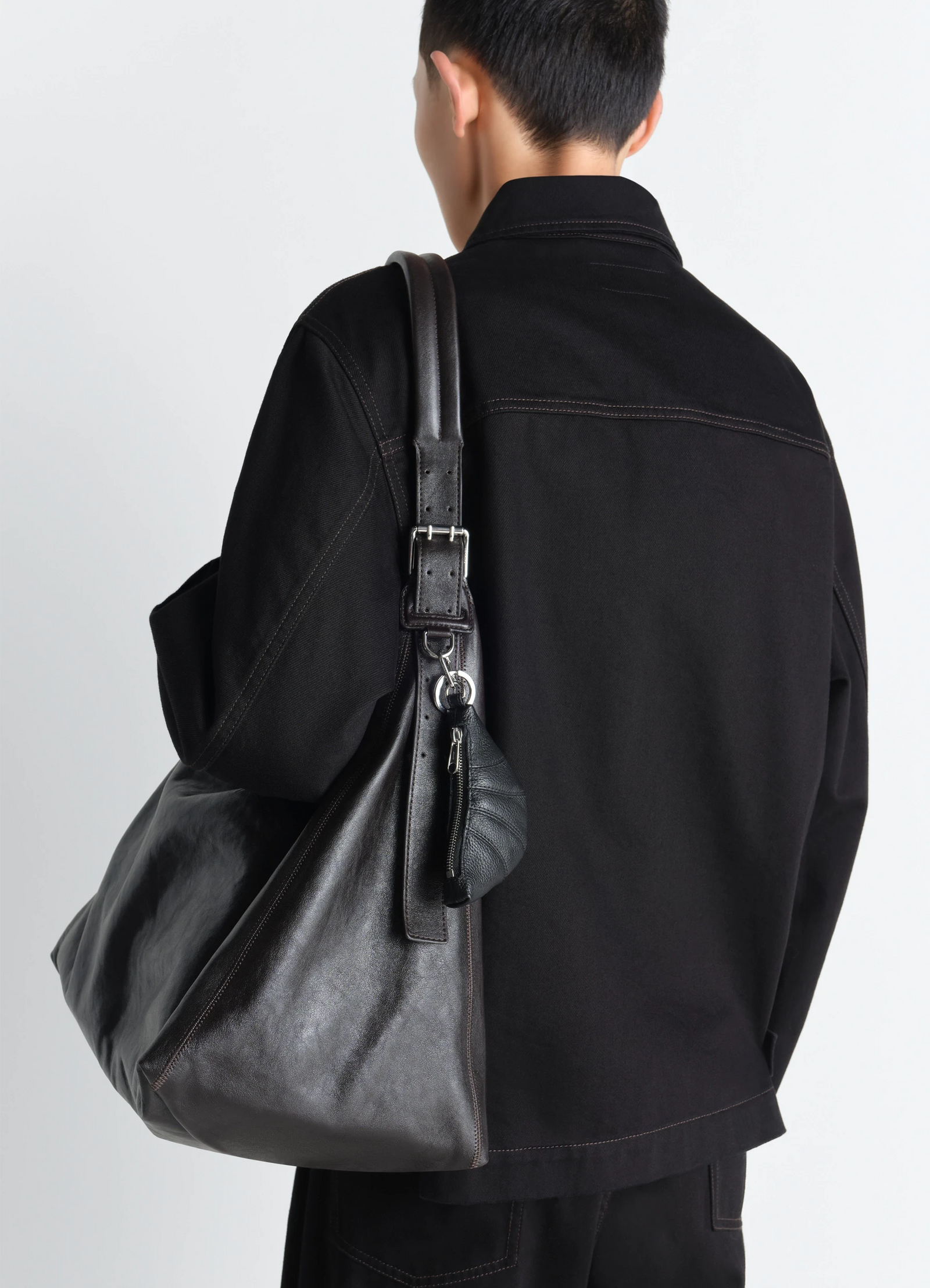 Mini croissant keyring in black grained leather, model shot, back view attached to shoulder bag