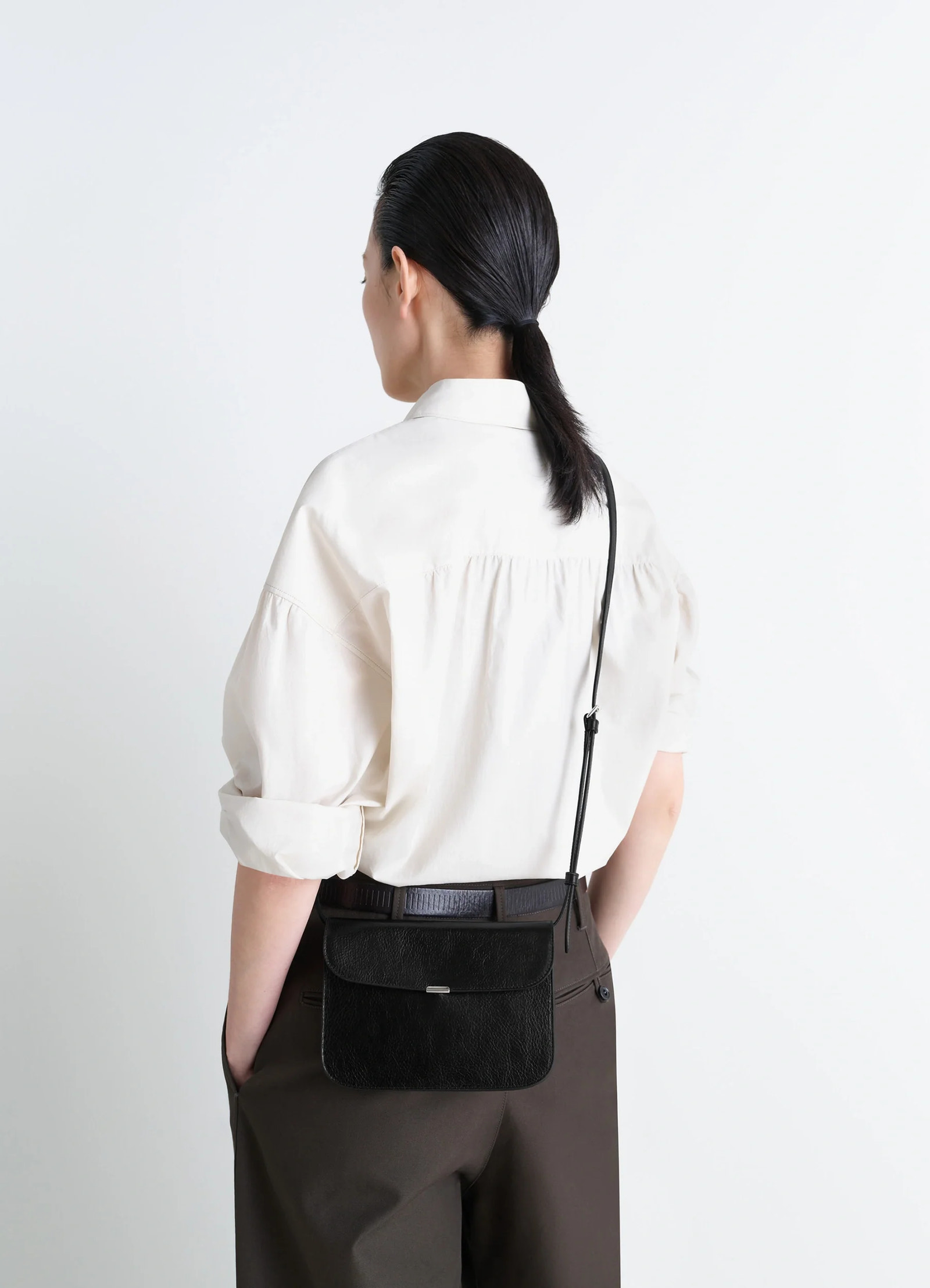 Soft tab wallet on strap in black leather, model shot, back view worn crossbody