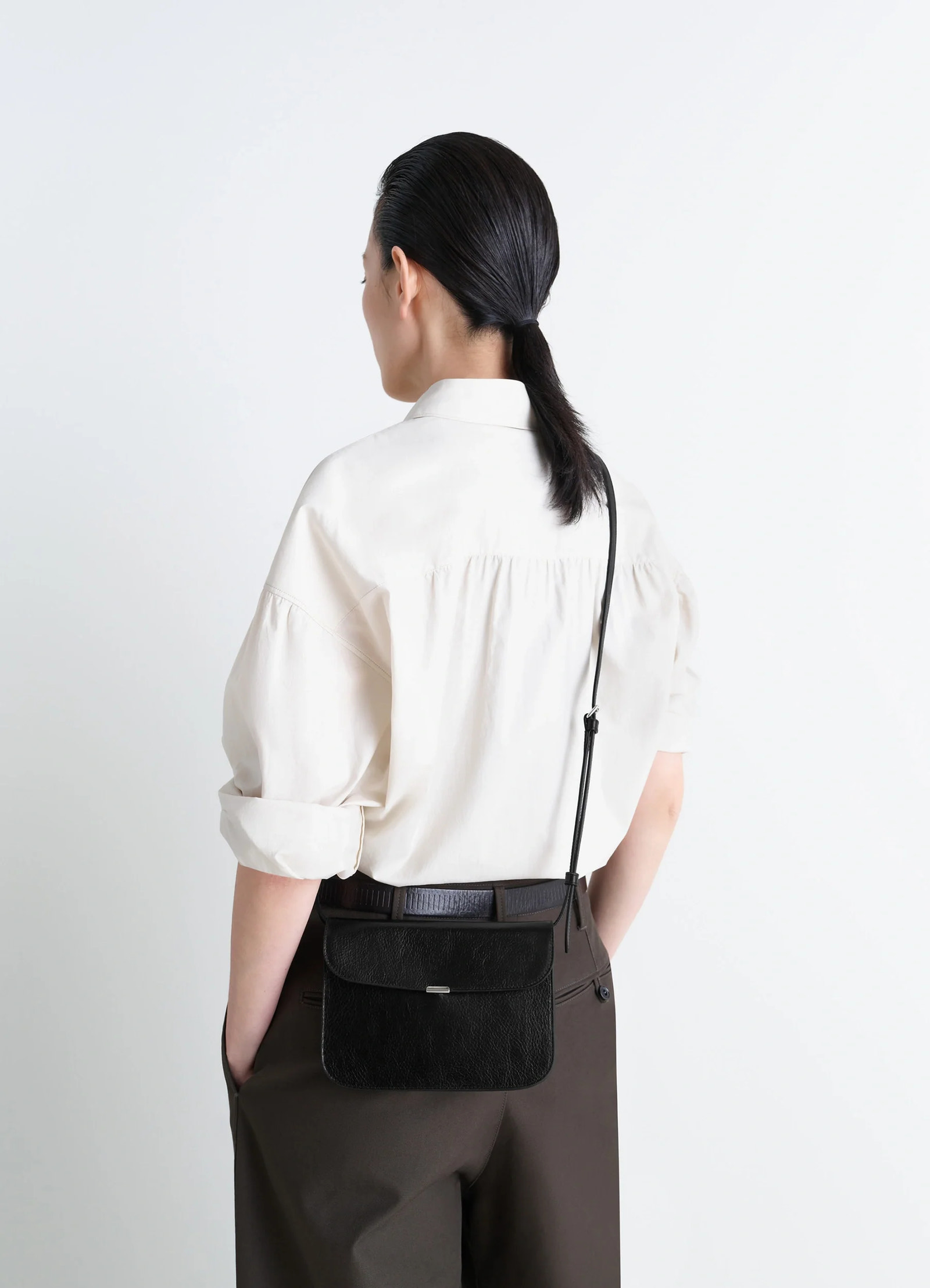 Soft tab wallet on strap in black leather, model shot, three-quarter rear shot hanging from shoulder