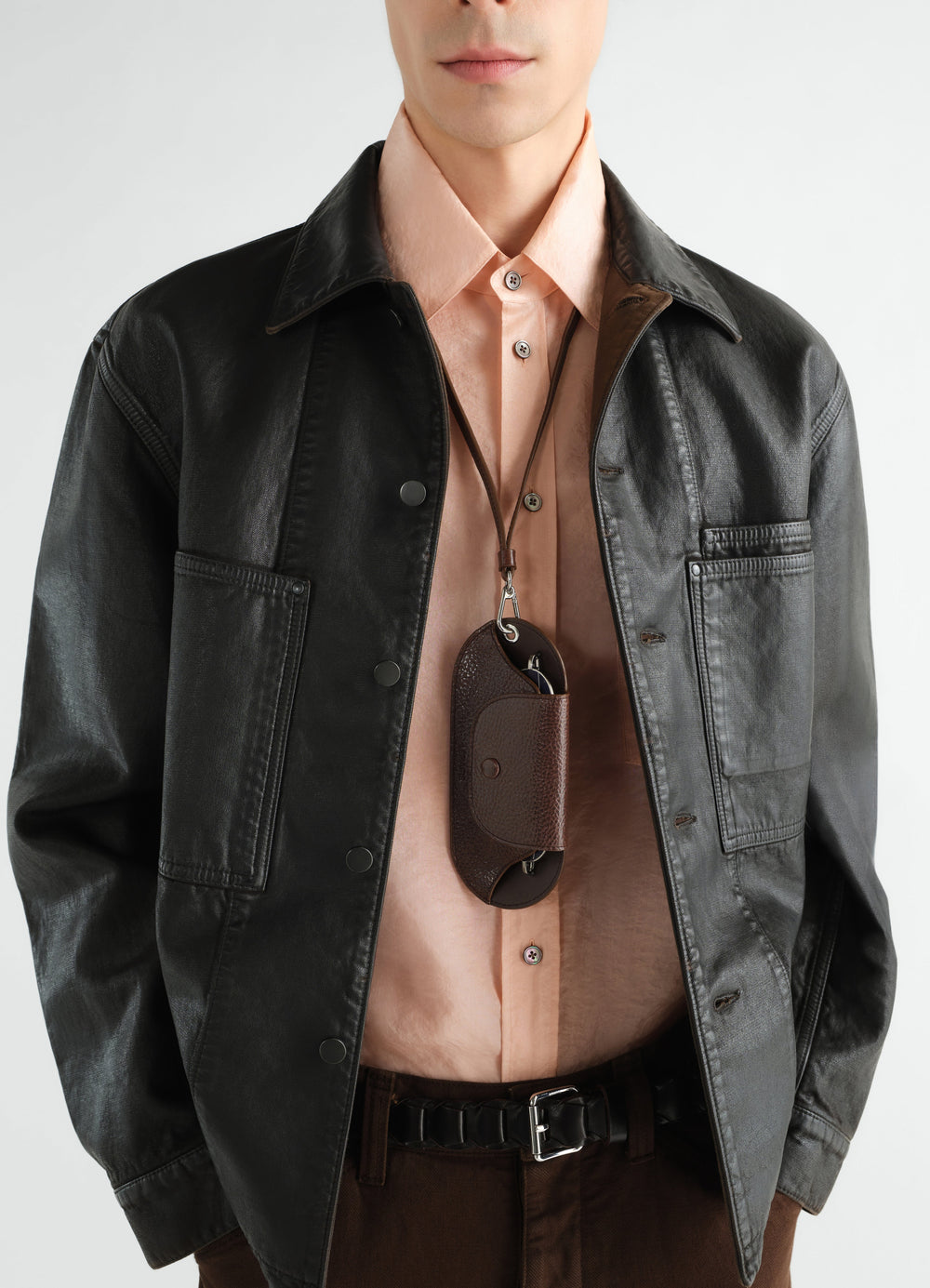 Glasses case in brown glossy vegetable-tanned leather by LEMAIRE worn by a model with a black leather jacket
