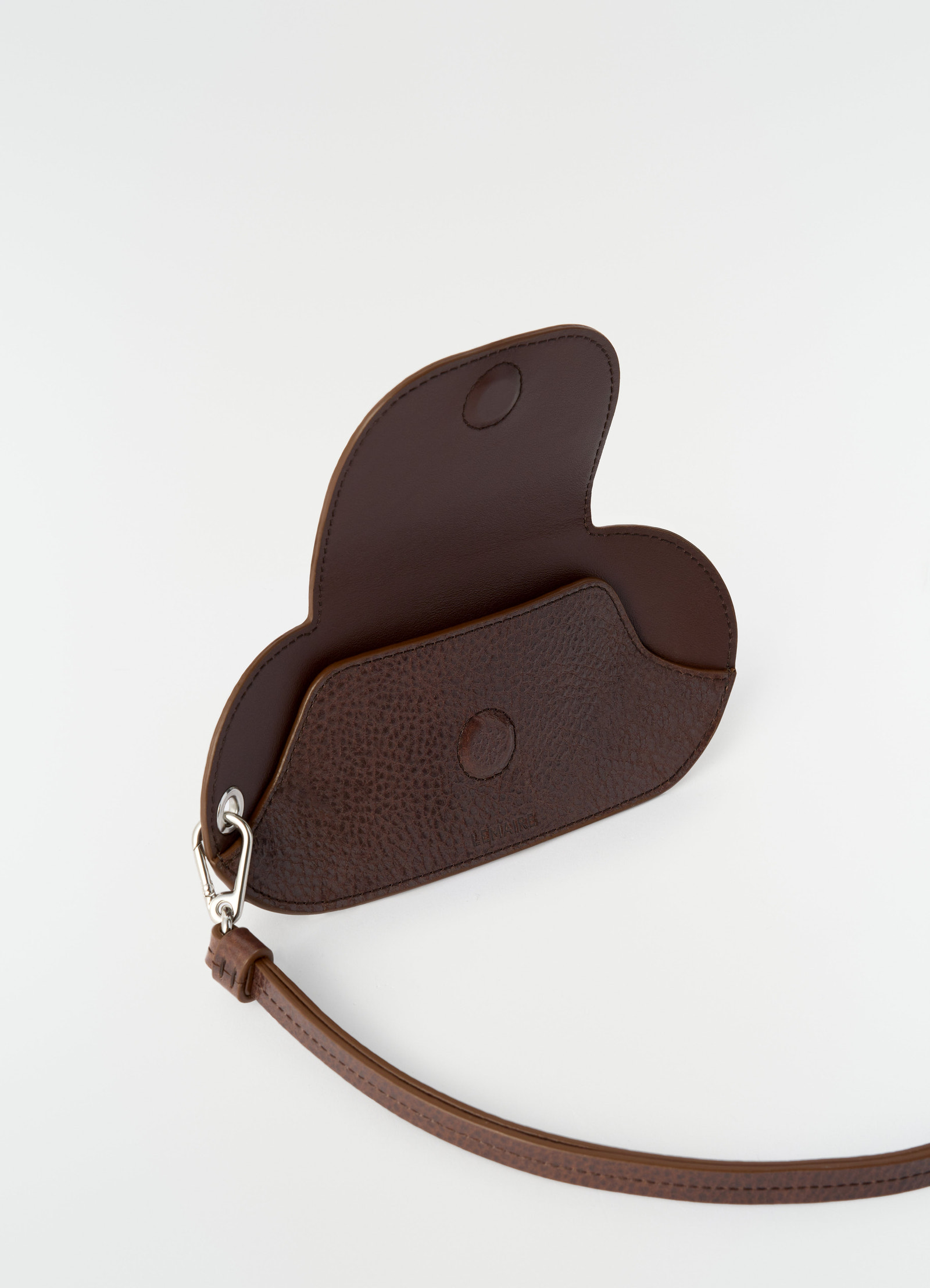 Glasses case in brown glossy vegetable-tanned leather by lemaire open with strap, styled on white background