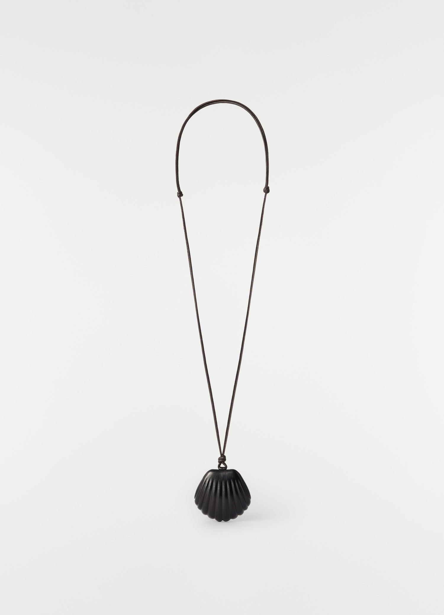 Shell mirror pendant in black patinated calfskin on long cord by LEMAIRE on plain white background