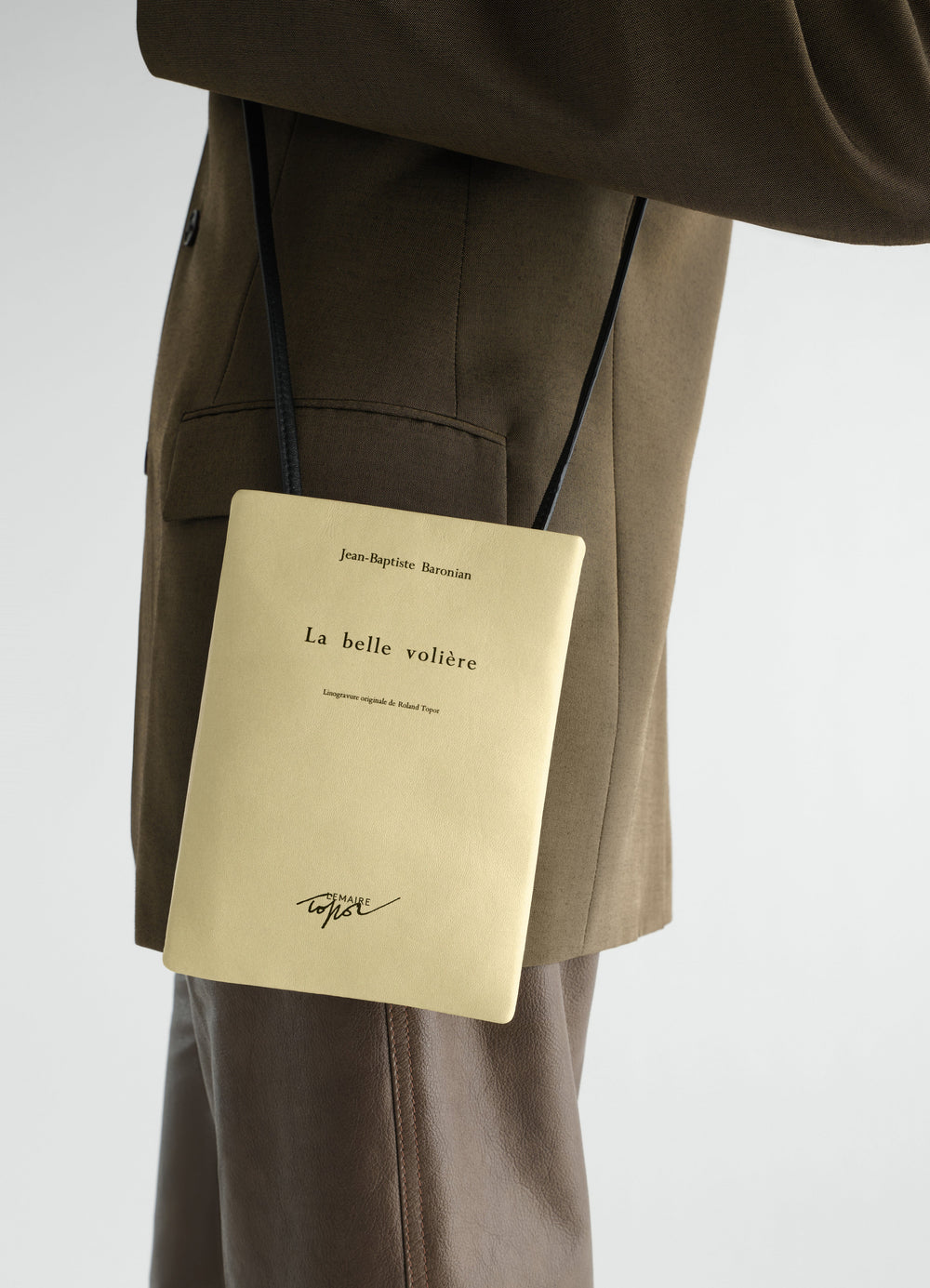 Small beige nappa leather book pouch with text print worn on side by model LEMAIRE