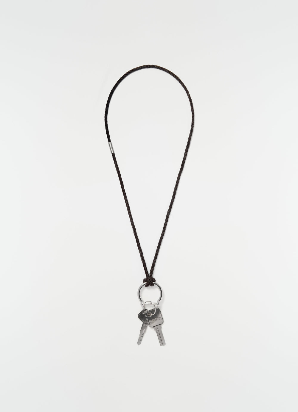 Keyring necklace with brown braided recycled leather cord and silver keys by LEMAIRE on plain white background