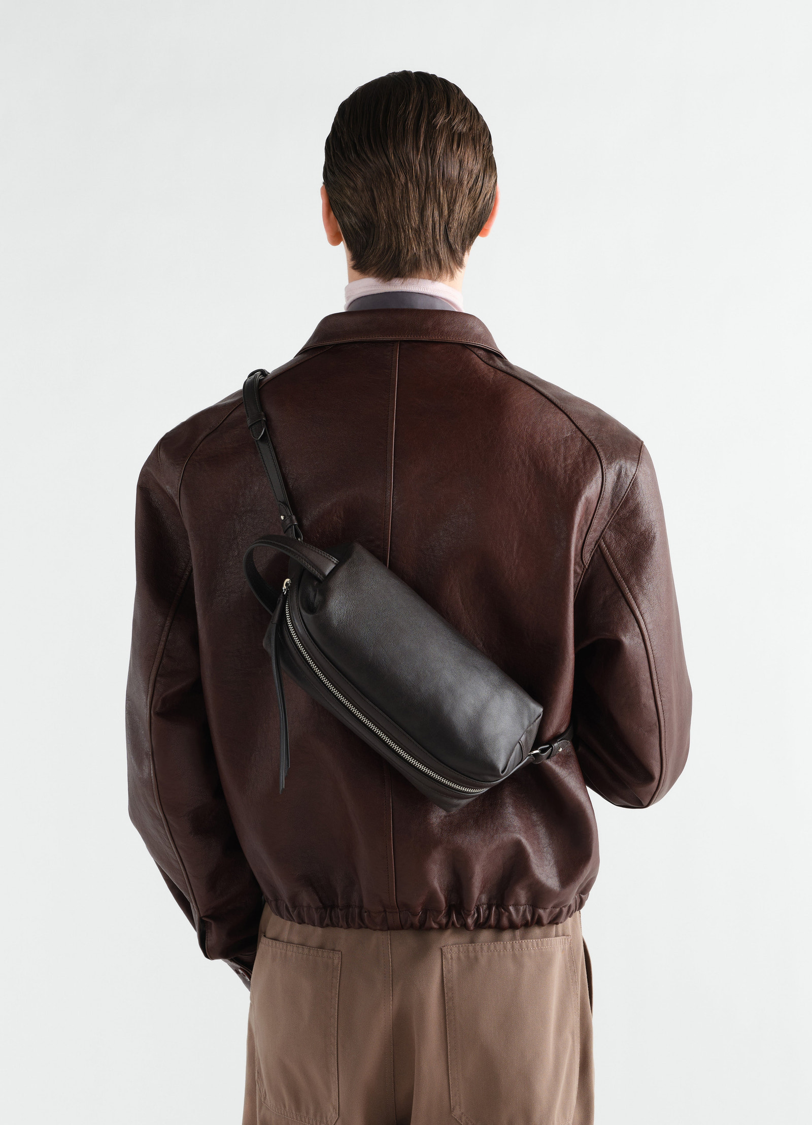 Small black nappa lambskin care bag lemaire worn crossbody on model back with dark brown leather jacket