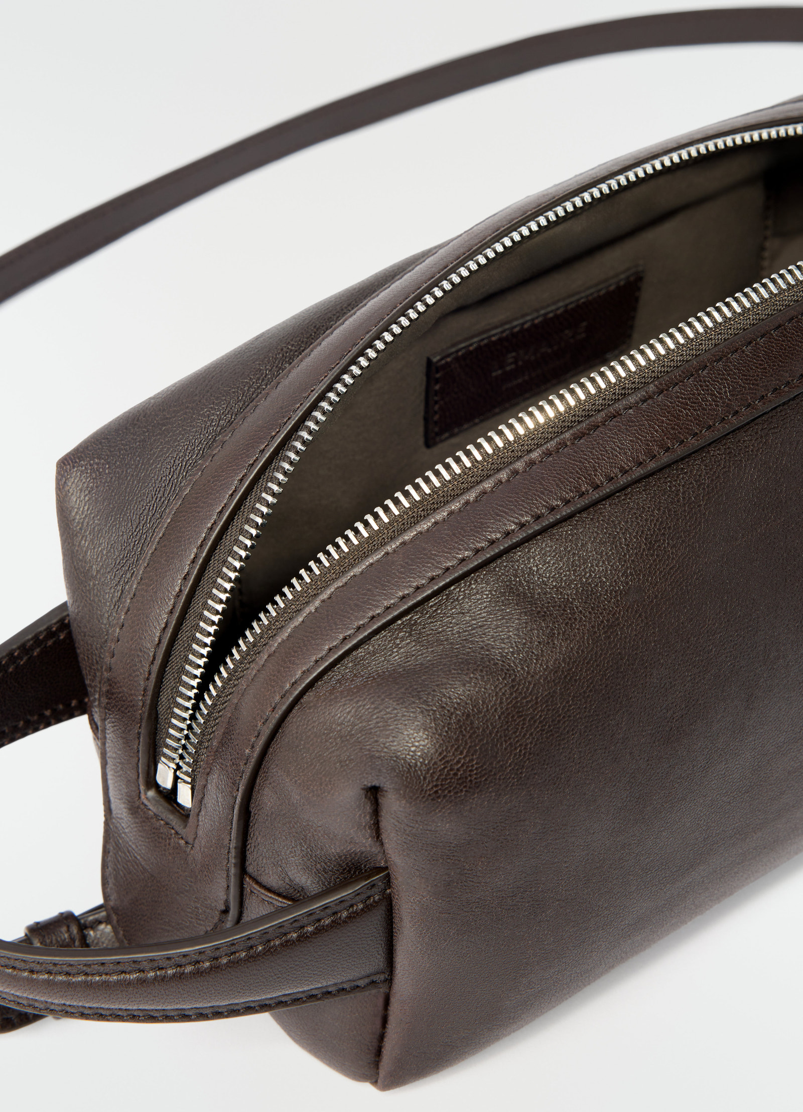 Small dark brown nappa lambskin care bag by lemaire with silver zipper close-up detail on white background
