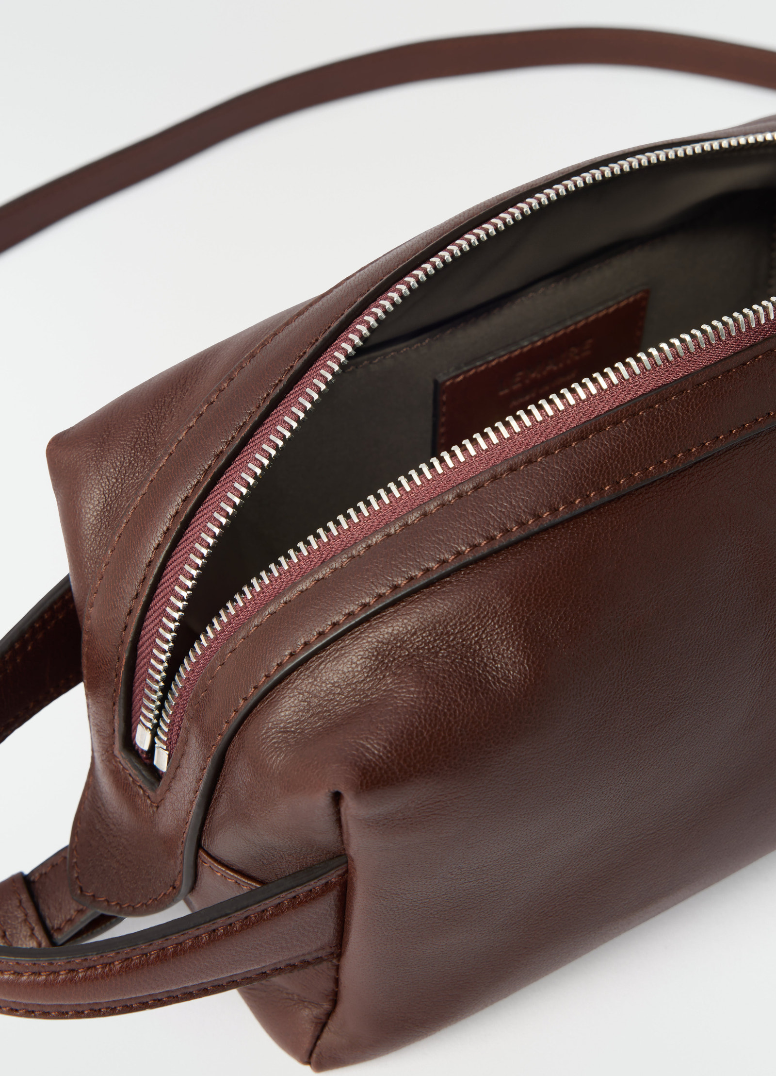 Small brown nappa lambskin care bag by lemaire with silver zipper close-up on plain white background