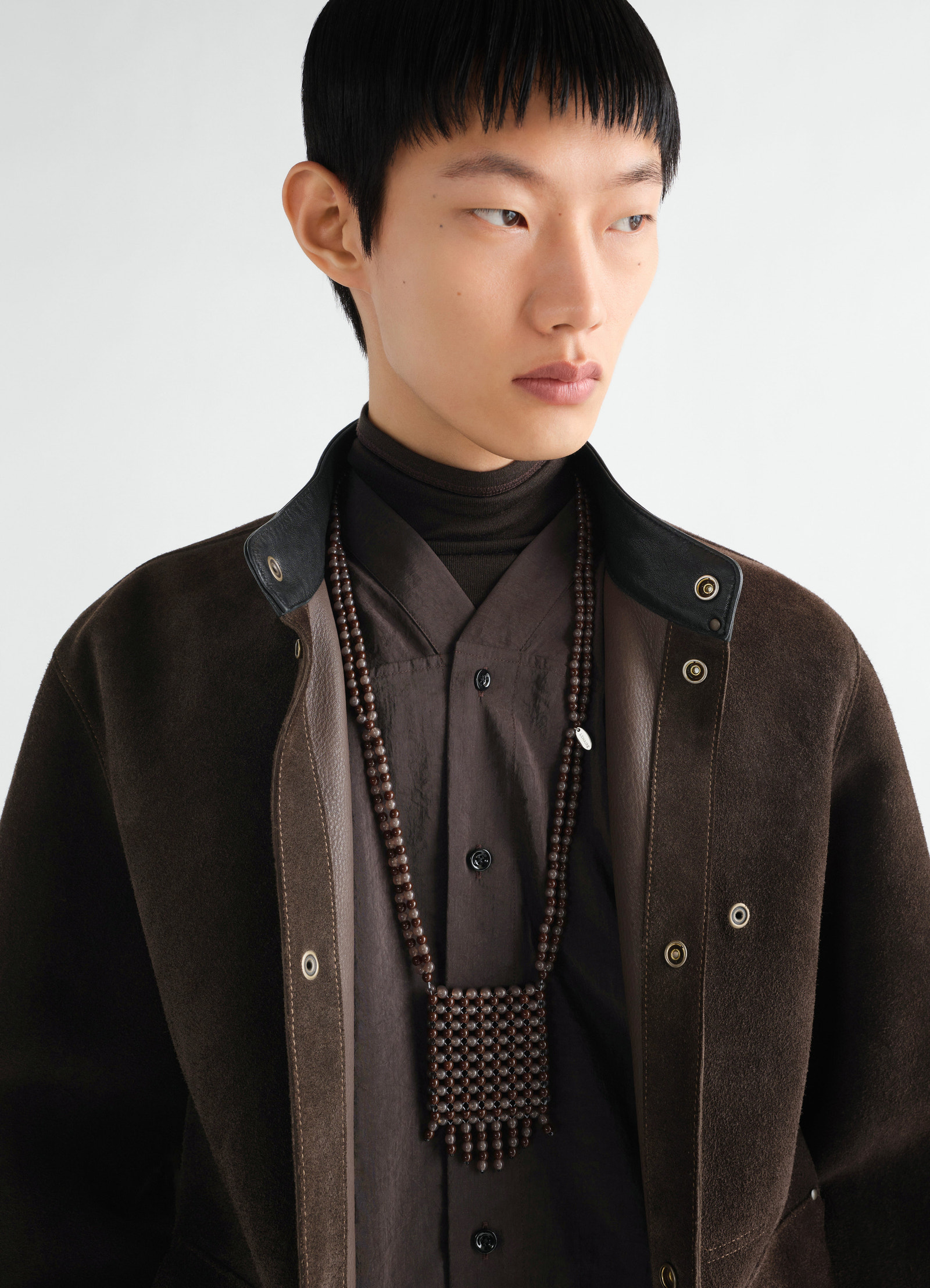 Grigri bag necklace in dark brown resin beads worn by a model styled with lemaire brown suede jacket and shirt