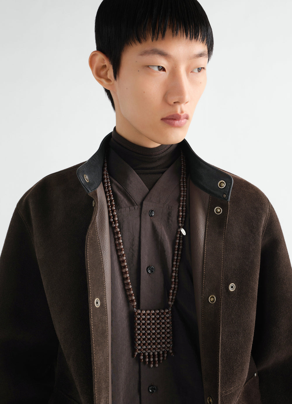 Grigri bag necklace in dark brown resin beads worn by a model styled with LEMAIRE brown suede jacket and shirt