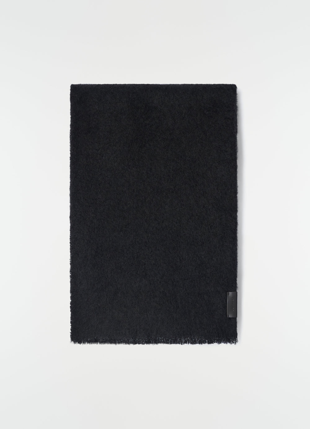 Fluffy black alpaca wool blend scarf by LEMAIRE laid flat with leather logo patch detail on white background