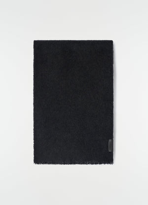 Fluffy black alpaca wool blend scarf by lemaire laid flat with leather logo patch detail on white background
