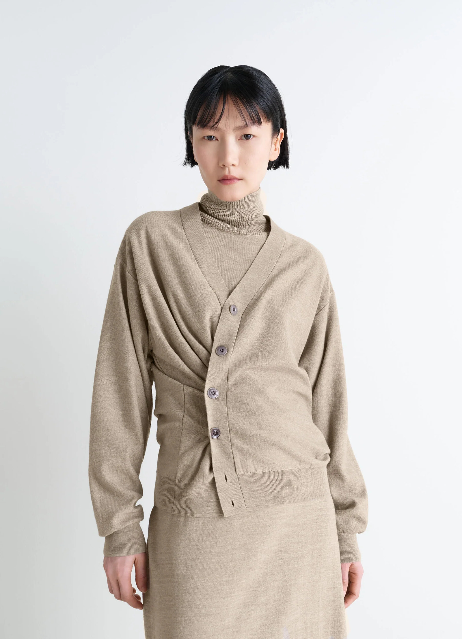 Lemaire relaxed twisted cardigan in light beige blended merino wool, model shot, three-quarter view draped waist detail