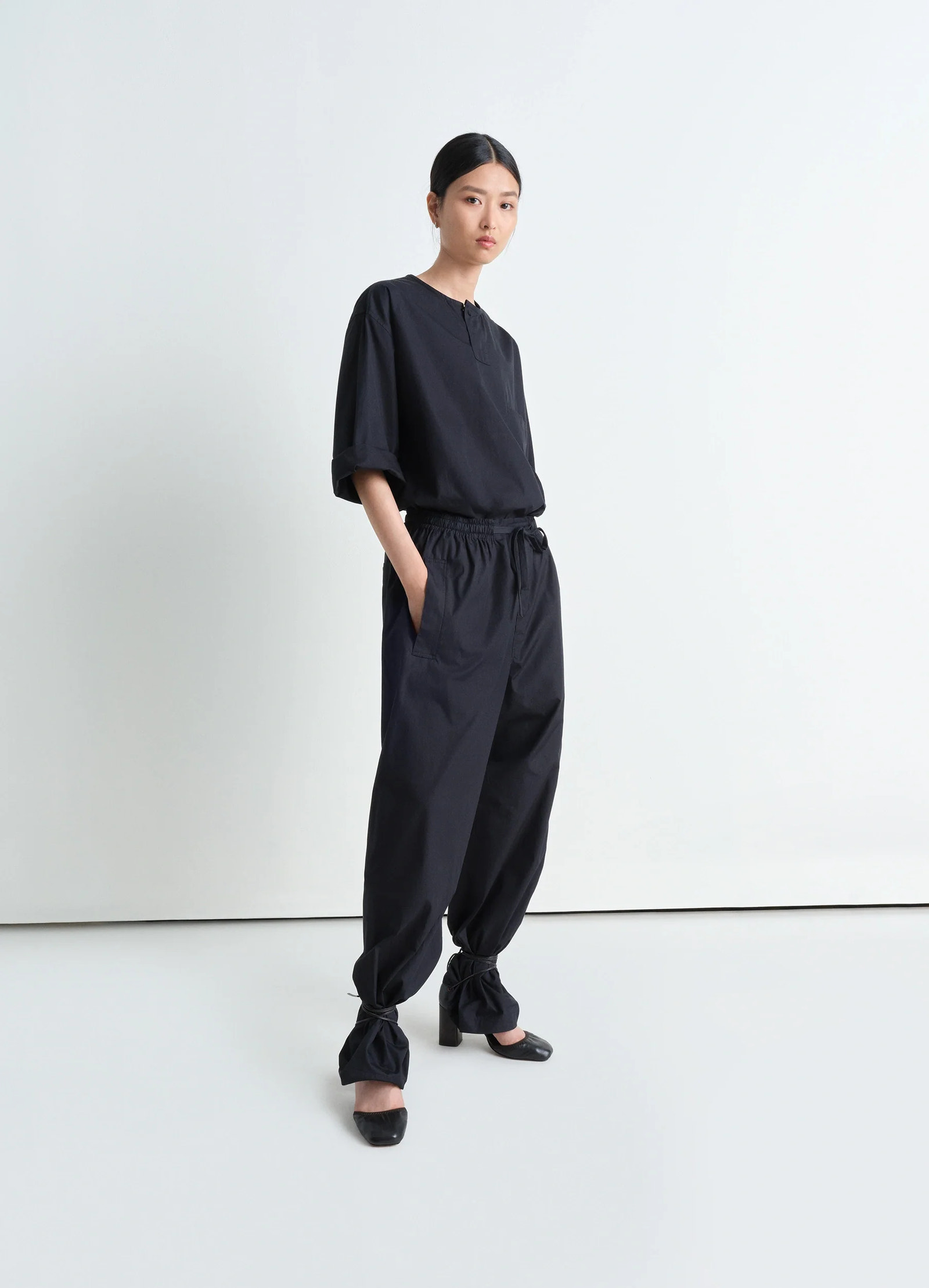 Short sleeve henley top in black heavy cotton poplin, model shot, semi-side view rolled sleeves, tucked in