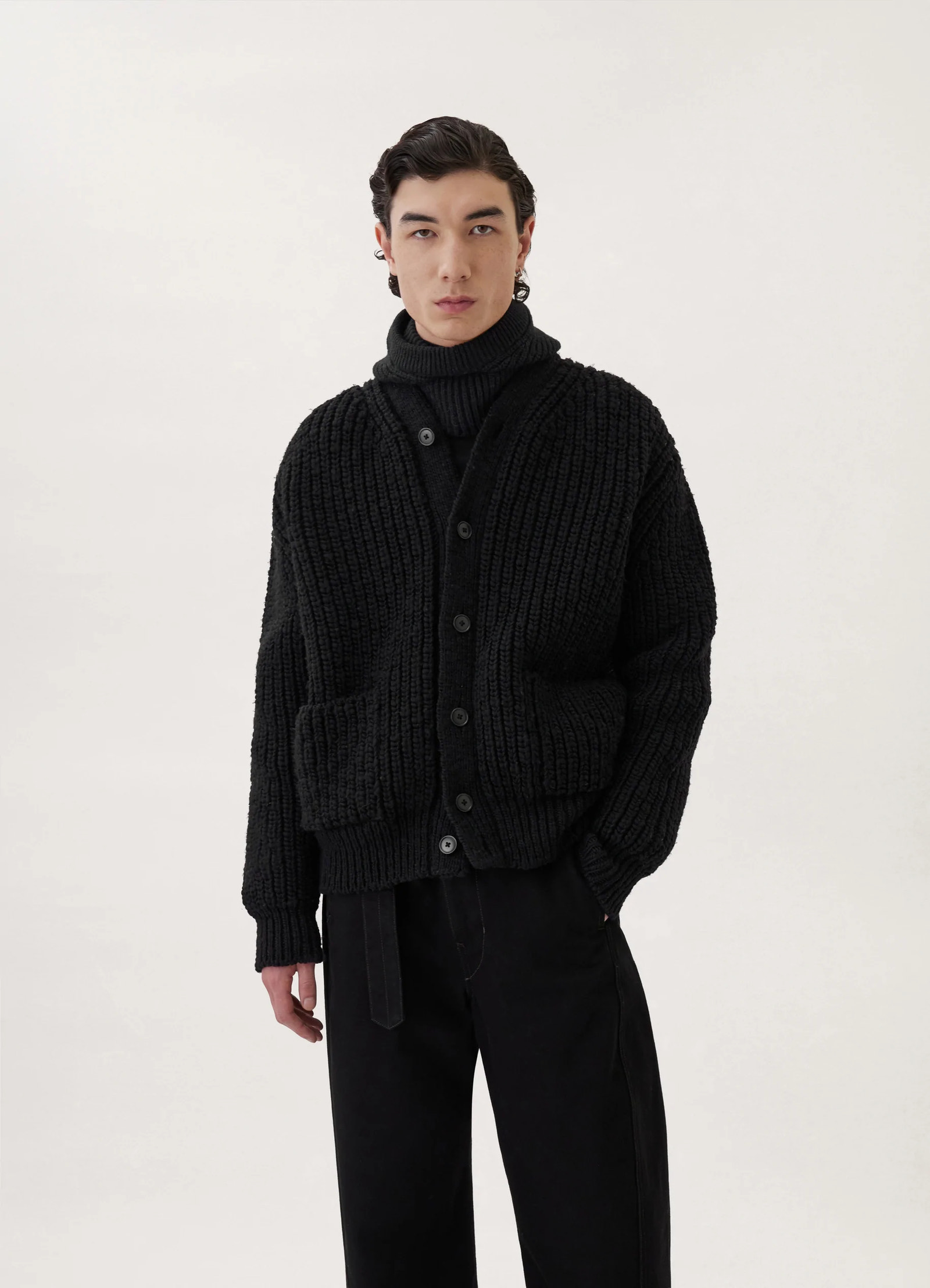 Chunky cardigan in black thick wool, model shot, three-quarter view front pockets ribbed texture