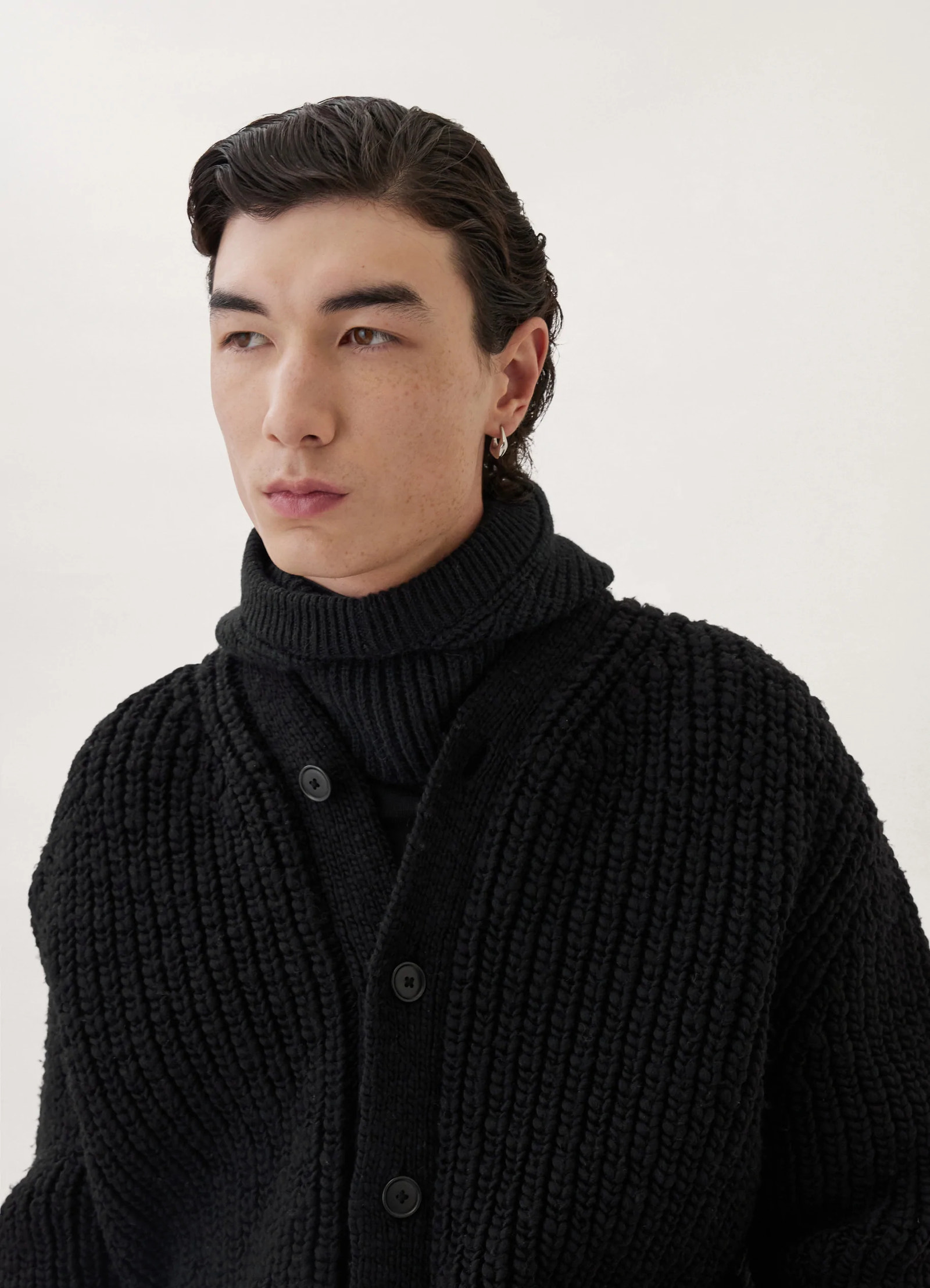 Chunky cardigan in black thick wool, model shot, side close-up view buttoned ribbed front