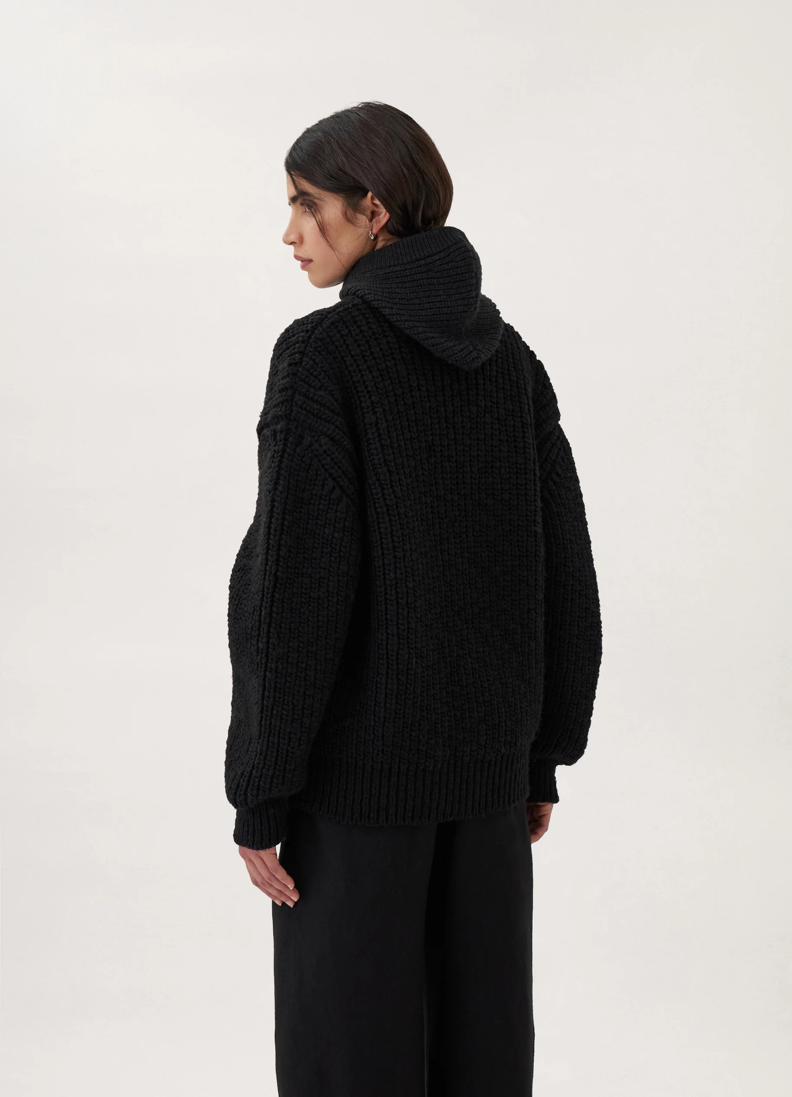 Chunky cardigan in black thick wool, model shot, backside three-quarter view hooded thick knit texture